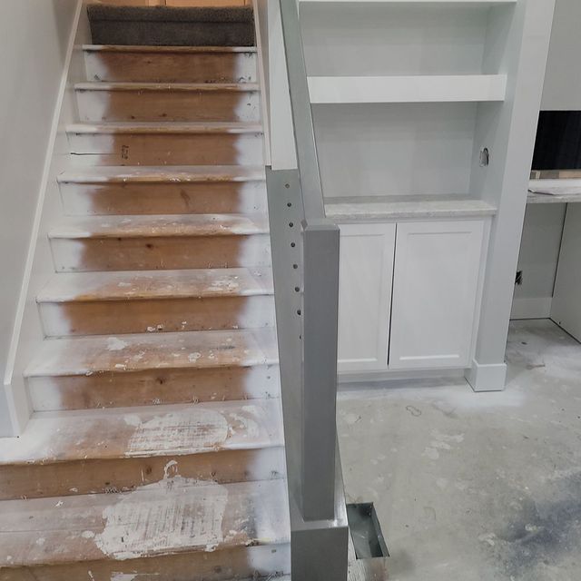 Staircase under renovation with visible wooden steps, partly painted white, and a gray railing.