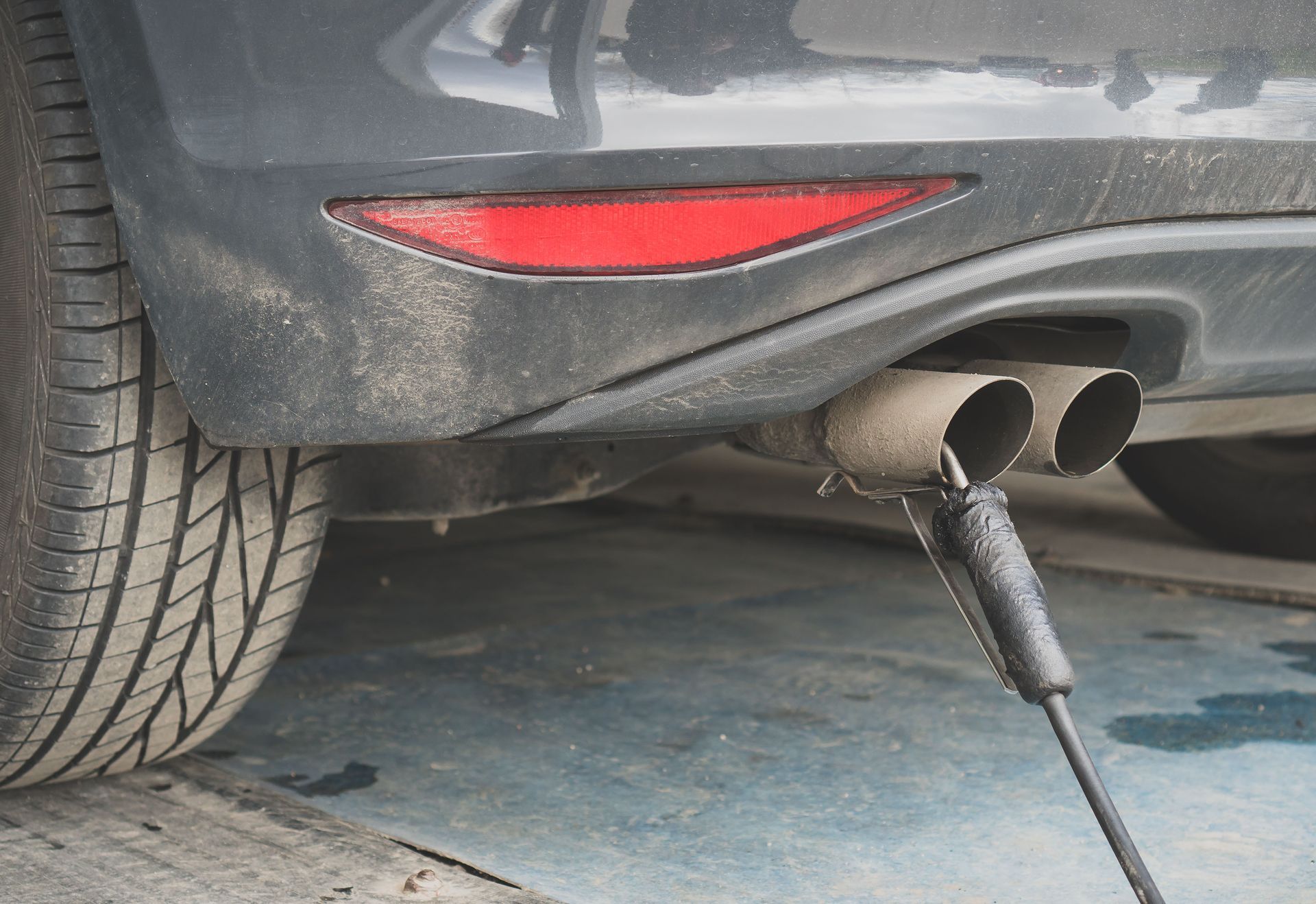 A probe inserted into a car’s dual exhaust pipe to measure vehicle emissions at a testing station.