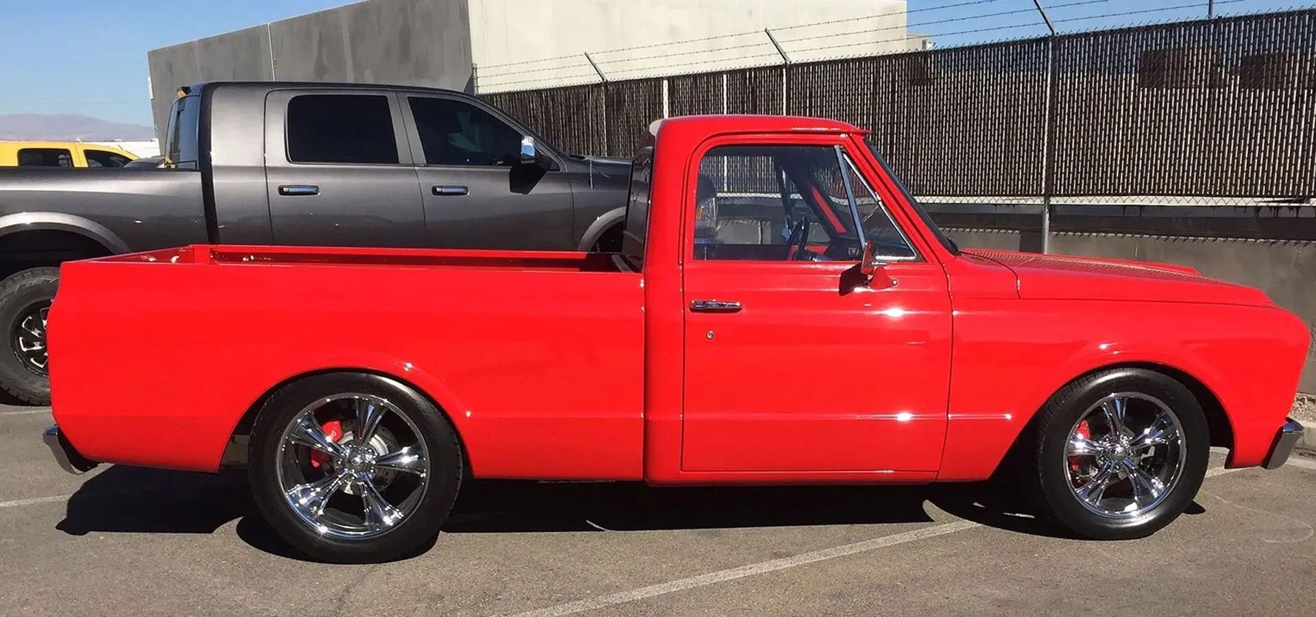 A bright red, lowered classic pickup truck parked outdoors, viewed from the side with chrome wheels.