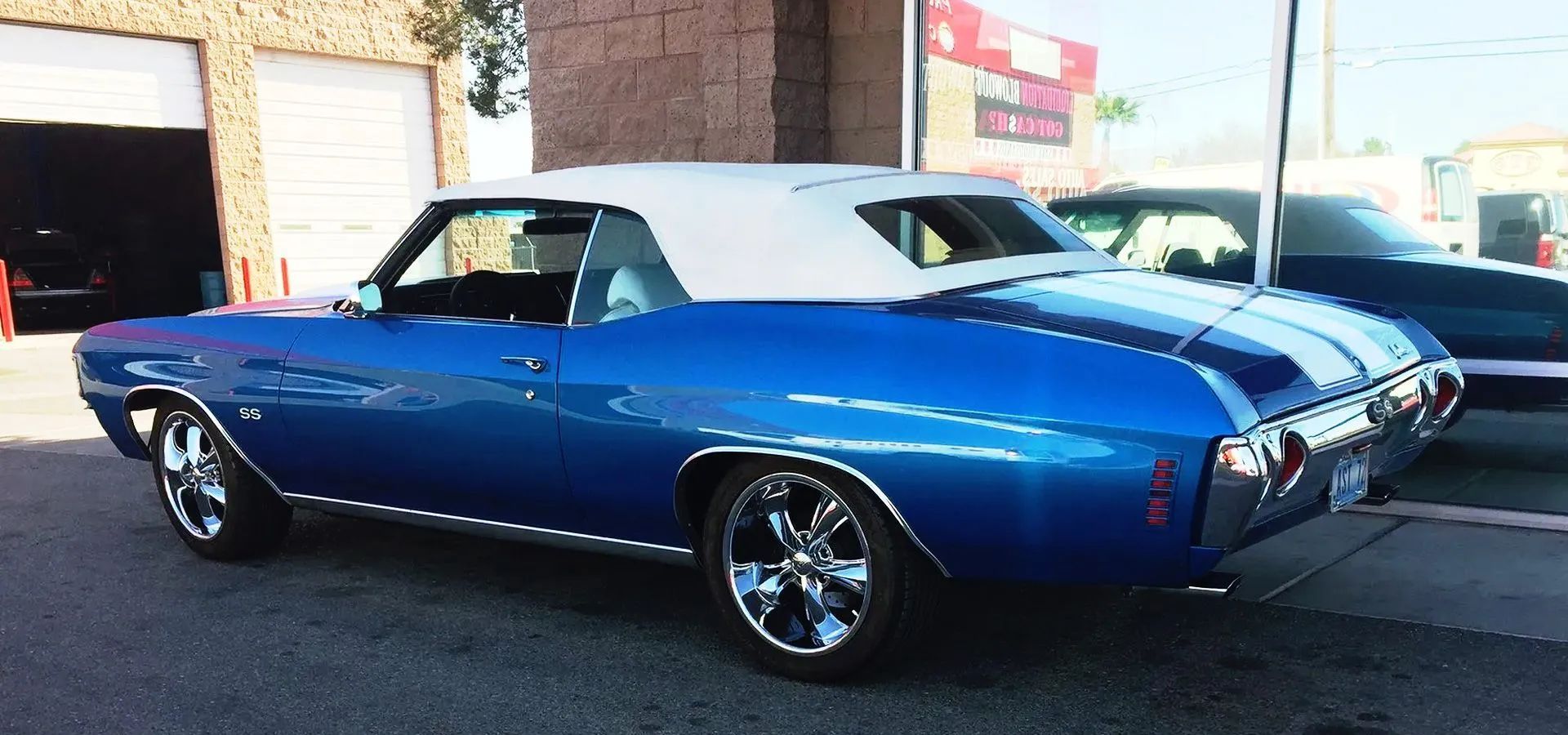 A bright blue Chevrolet Chevelle convertible with a white roof and racing stripes, parked on a paved lot.