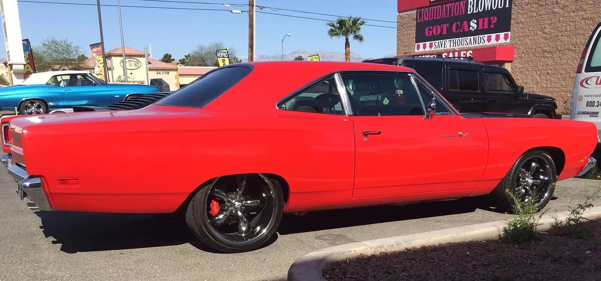 A red, vintage muscle car parked in a parking lot on a sunny day.