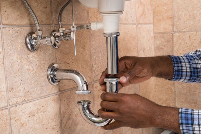 Hands installing a chrome sink drain pipe beneath a bathroom sink