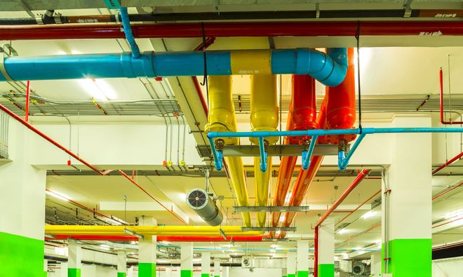 Color-coded industrial ceiling pipes and ducts in a brightly lit mechanical room