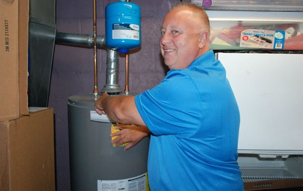 Man in blue shirt adjusting a water heater in a utility room
