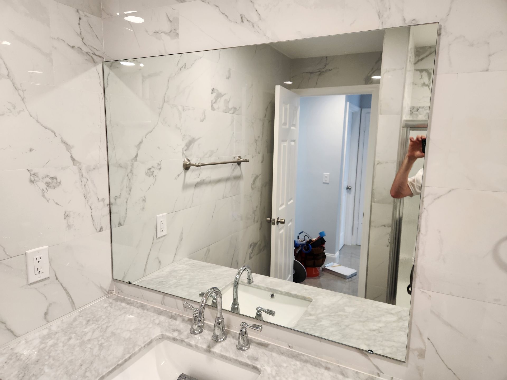 Bathroom with marble walls and countertop, large mirror above the sink, reflected view of a hallway.