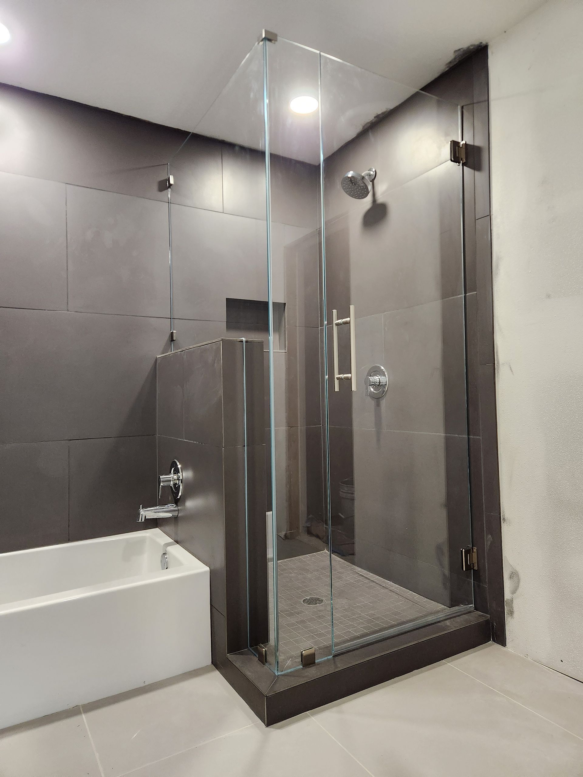 Modern bathroom with glass shower enclosure, bathtub, and gray tiled walls.