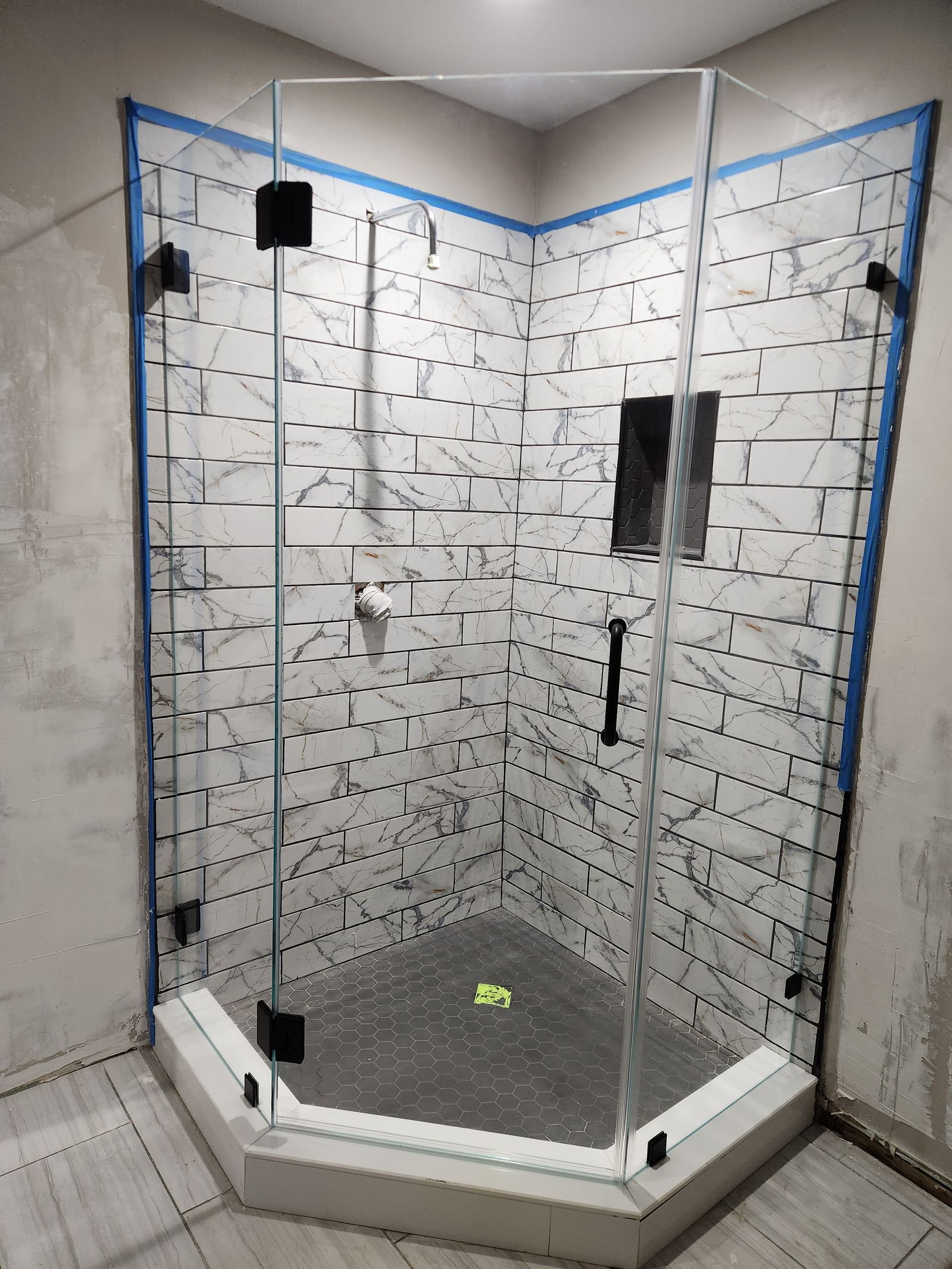 A glass shower enclosure with black hardware, set in a bathroom with marble-style tiles.