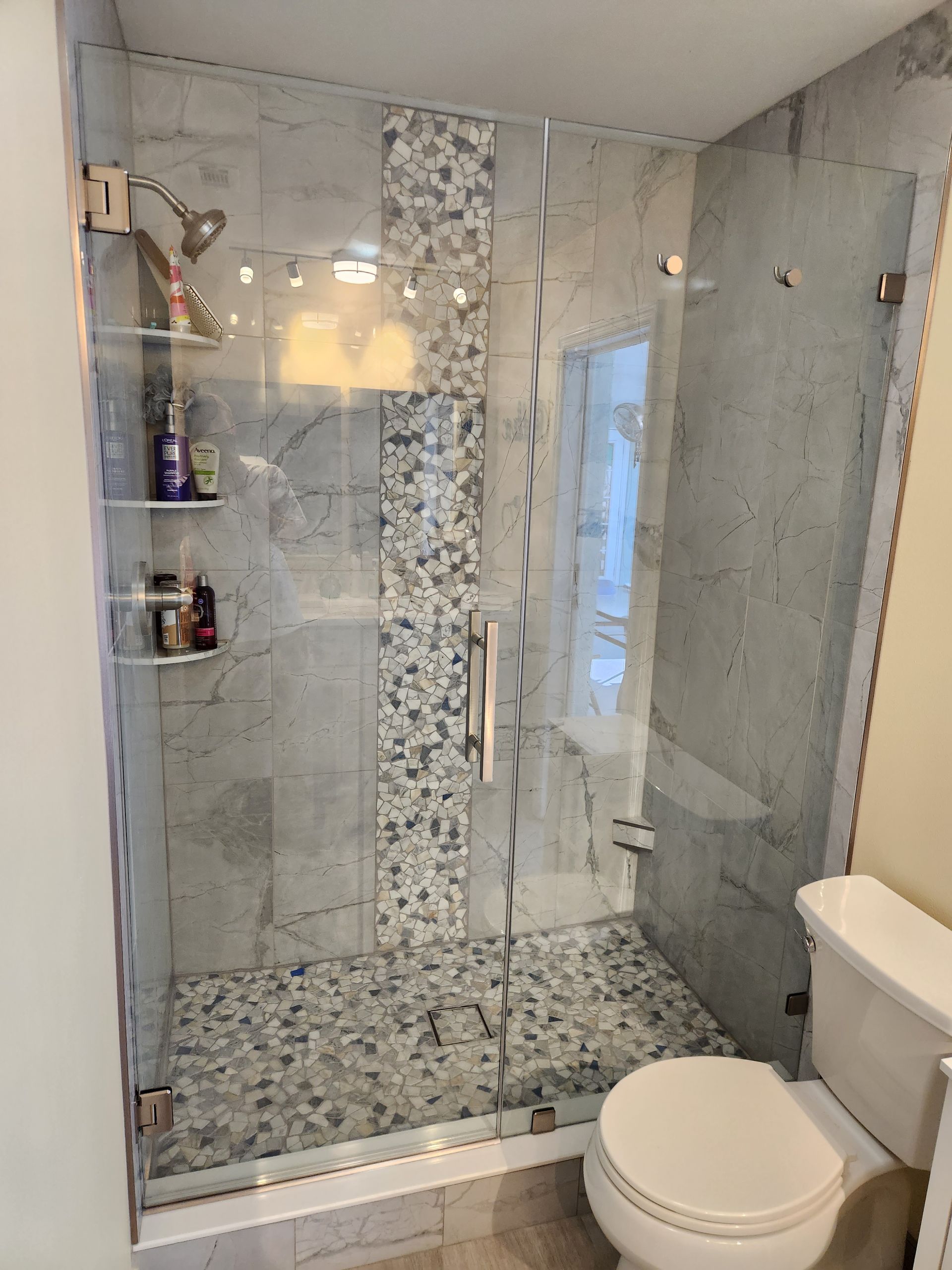 Modern bathroom with a marble-tiled shower, pebble floor, glass door, and a white toilet.