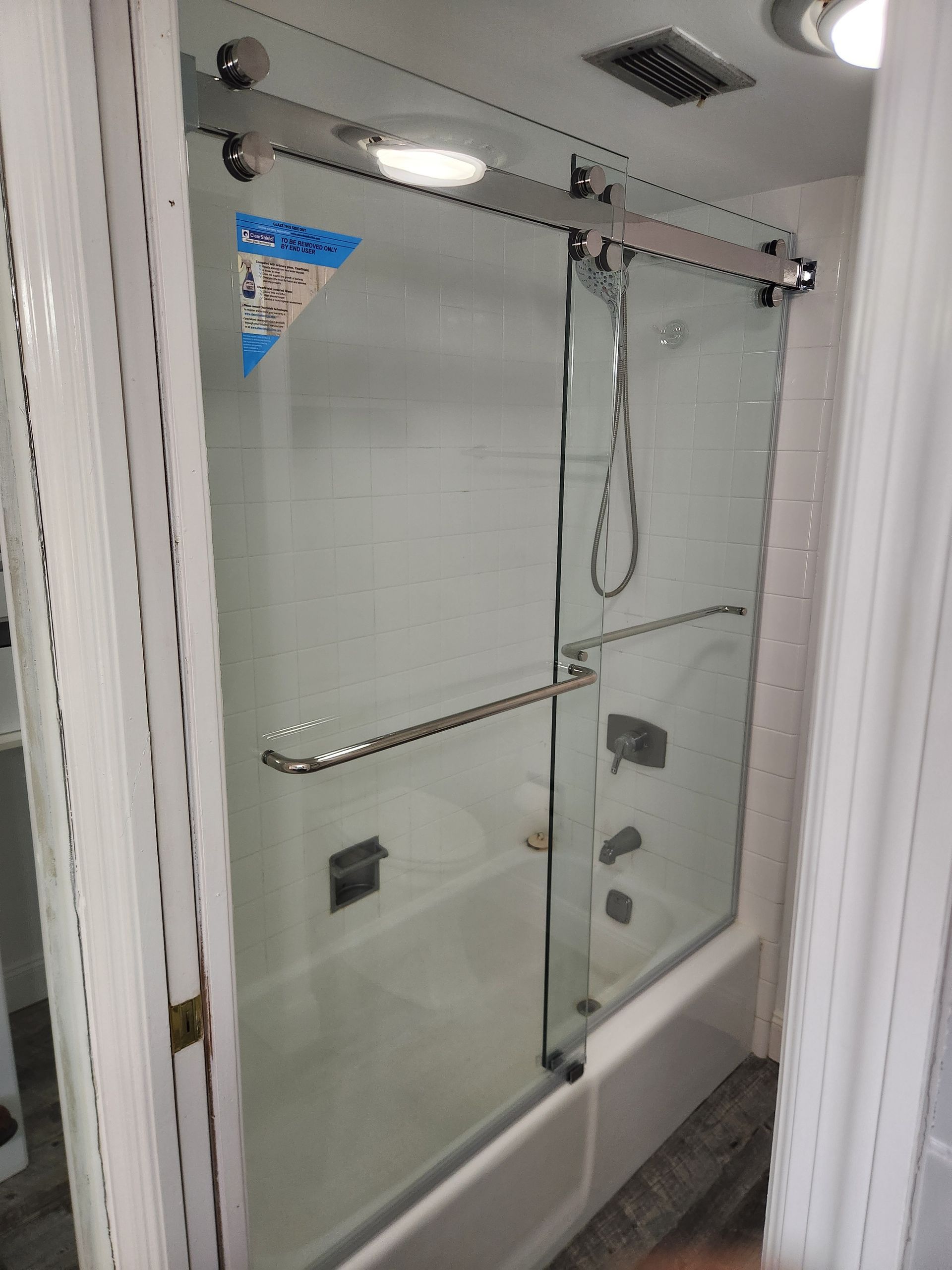 Shower with a glass door, chrome hardware, and a showerhead. The setting is a bathroom.