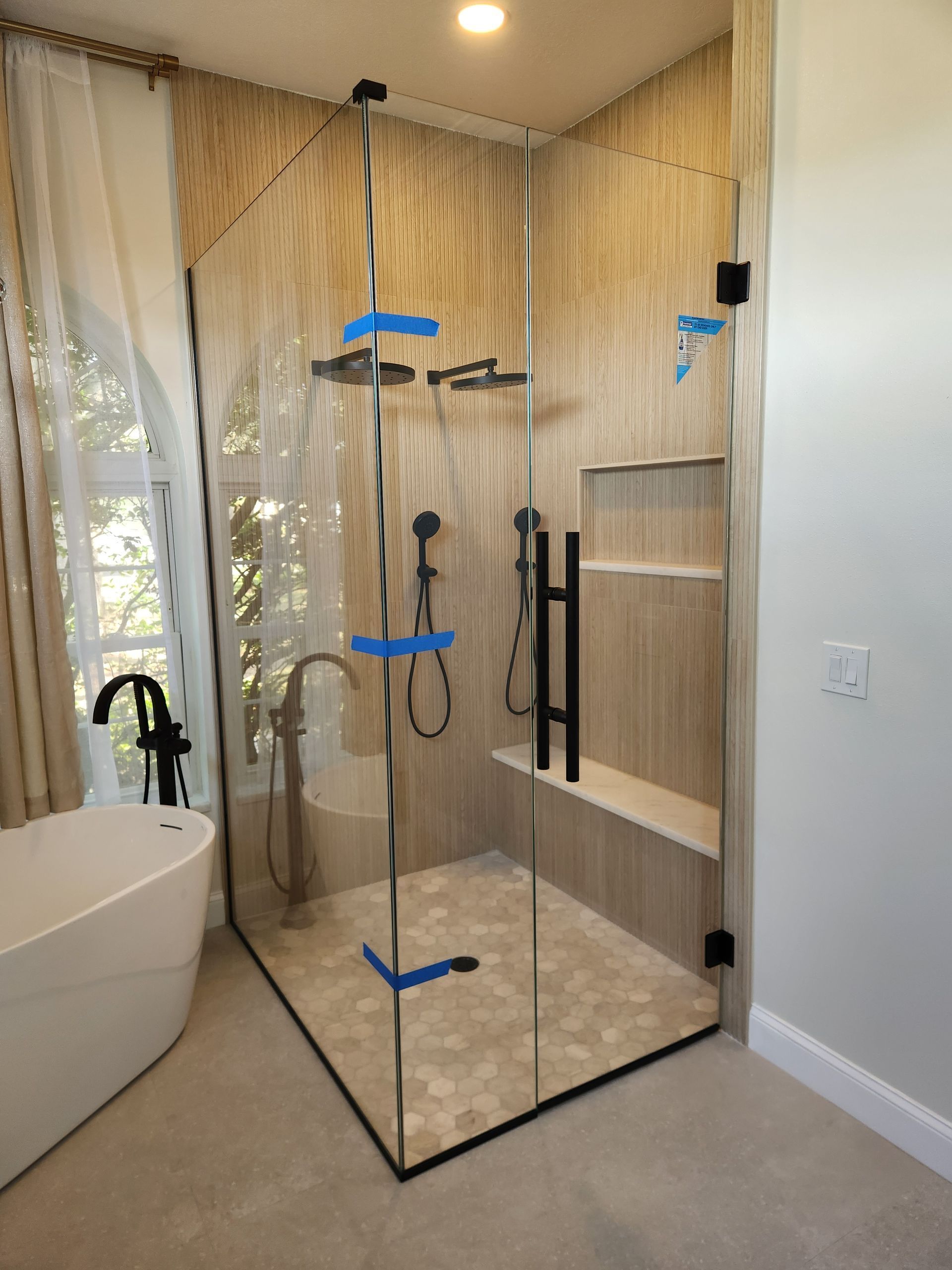 Modern bathroom with a glass shower enclosure, a white tub, and neutral-toned tiles and walls.