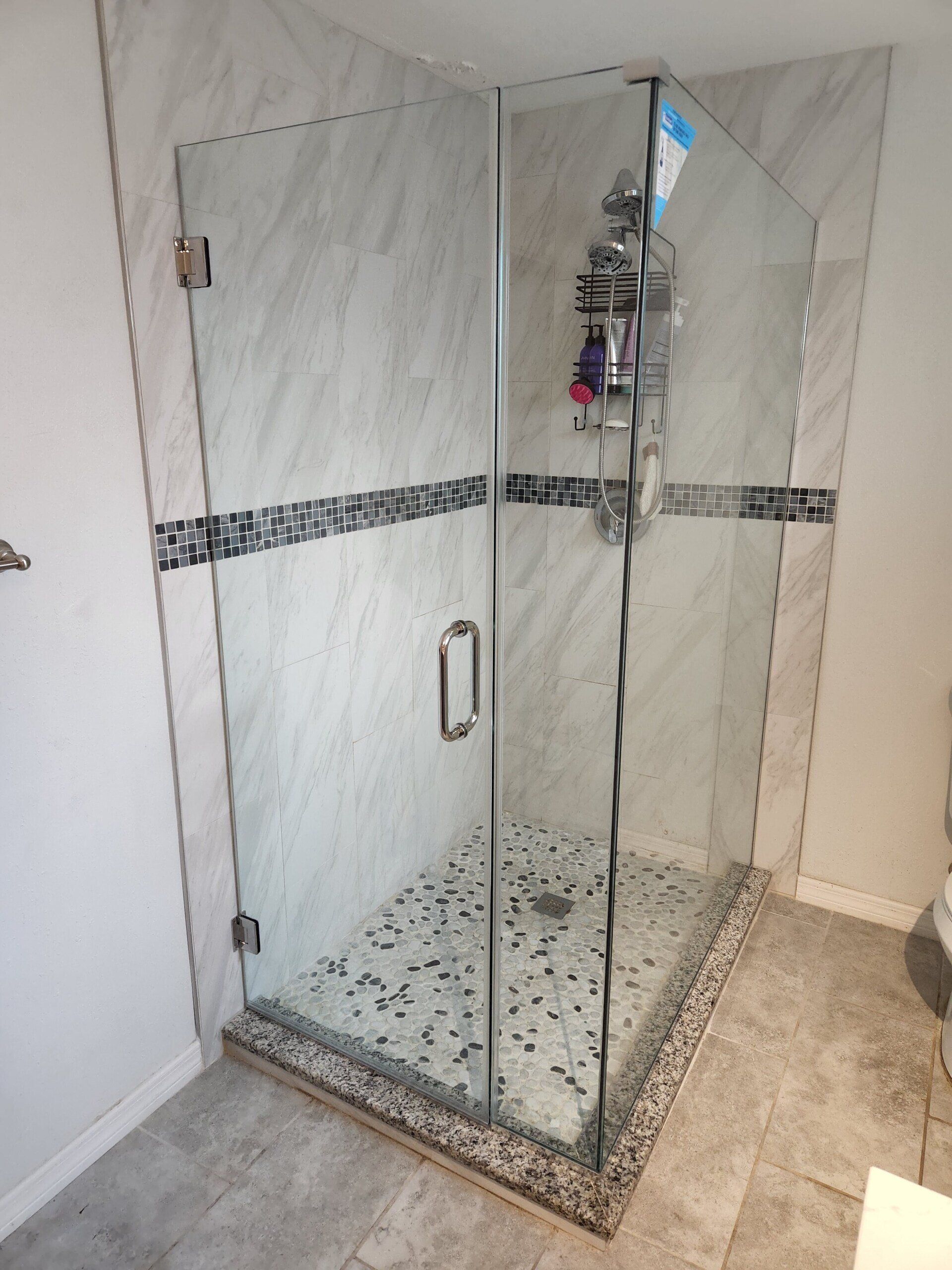 Glass shower enclosure with marble-look walls and mosaic tile accent. Includes a glass door, chrome fixtures, and stone floor.
