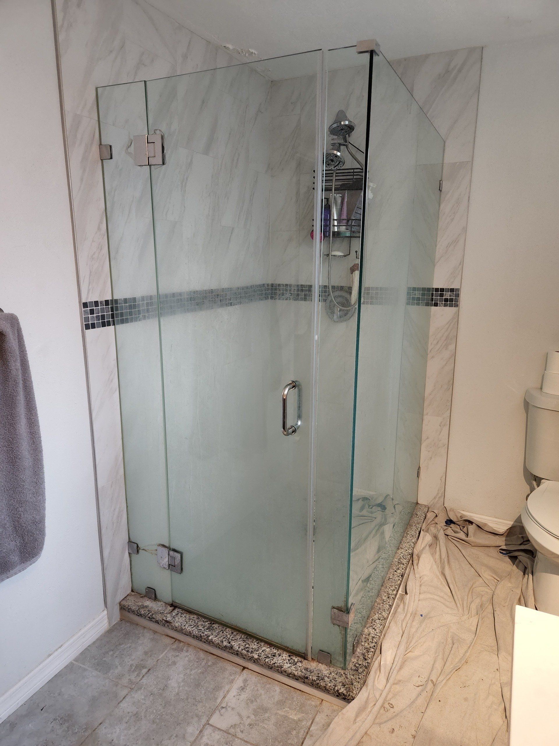 Glass shower enclosure with marble walls and floor, chrome hardware.