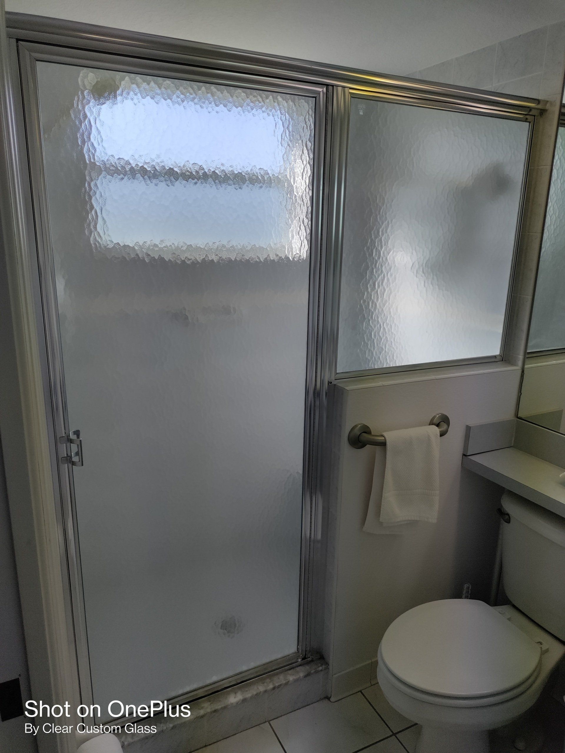 Shower with frosted glass door, toilet, towel rack in a bathroom.