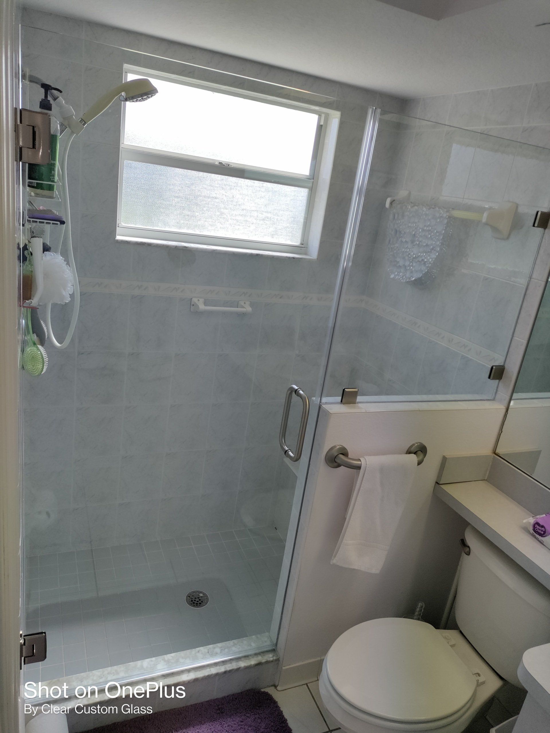 Bathroom with glass shower door, white tiles, a window, and a toilet.