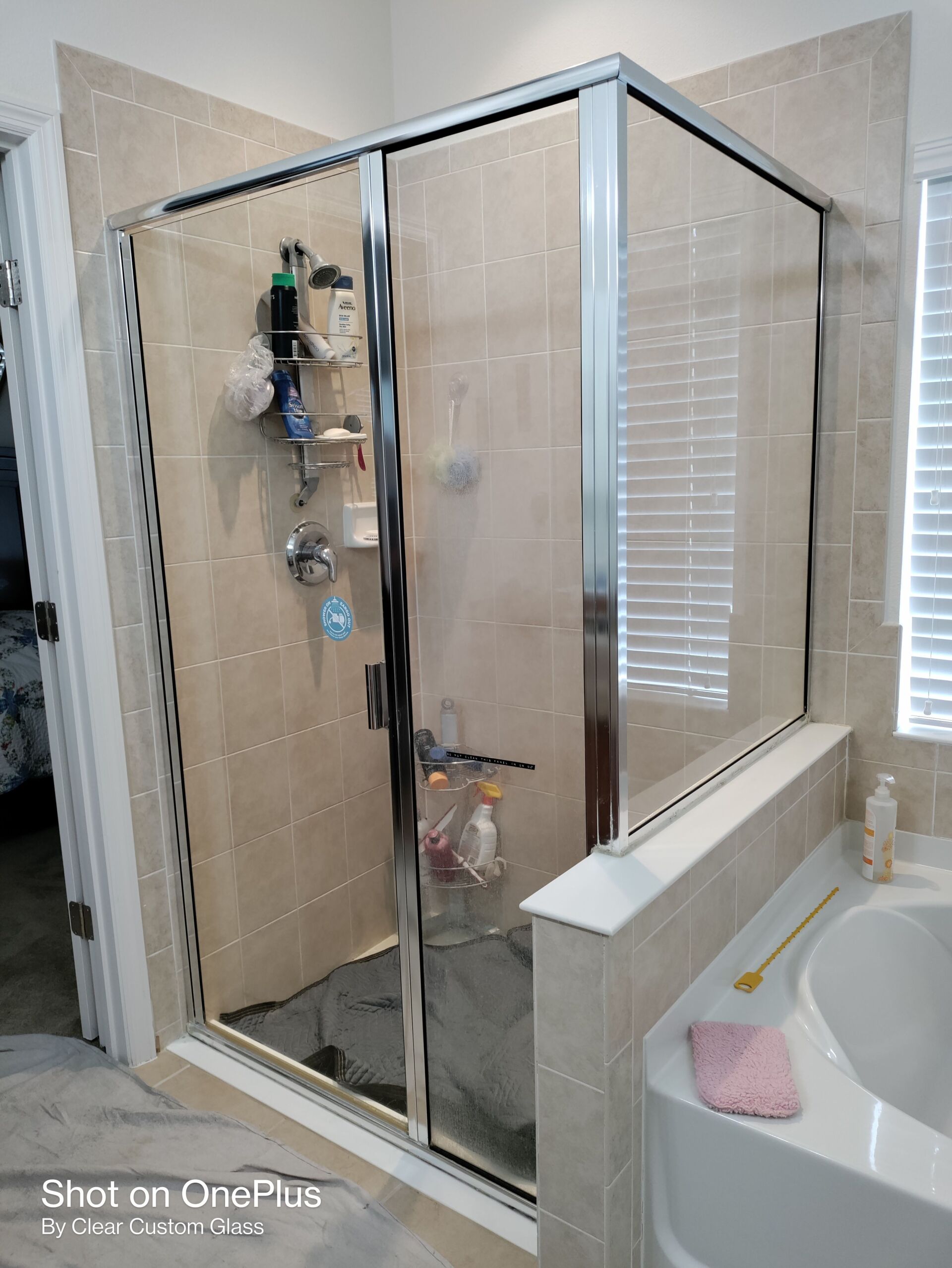 Shower with a glass door, chrome frame, and beige tile. Tub is on the right.