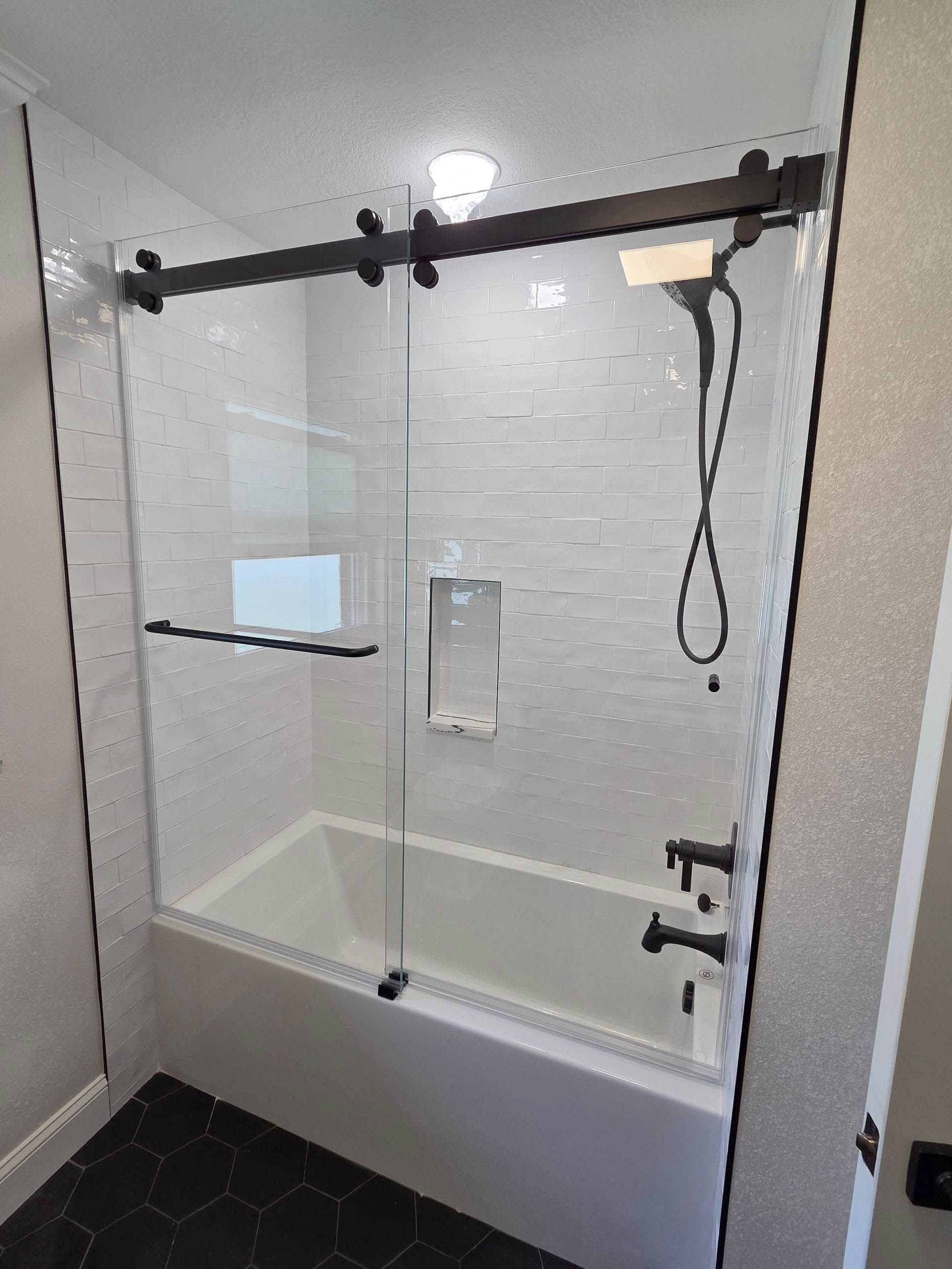 Empty tiled bathroom with a walk-in shower, black grab bar, and hand-held showerhead