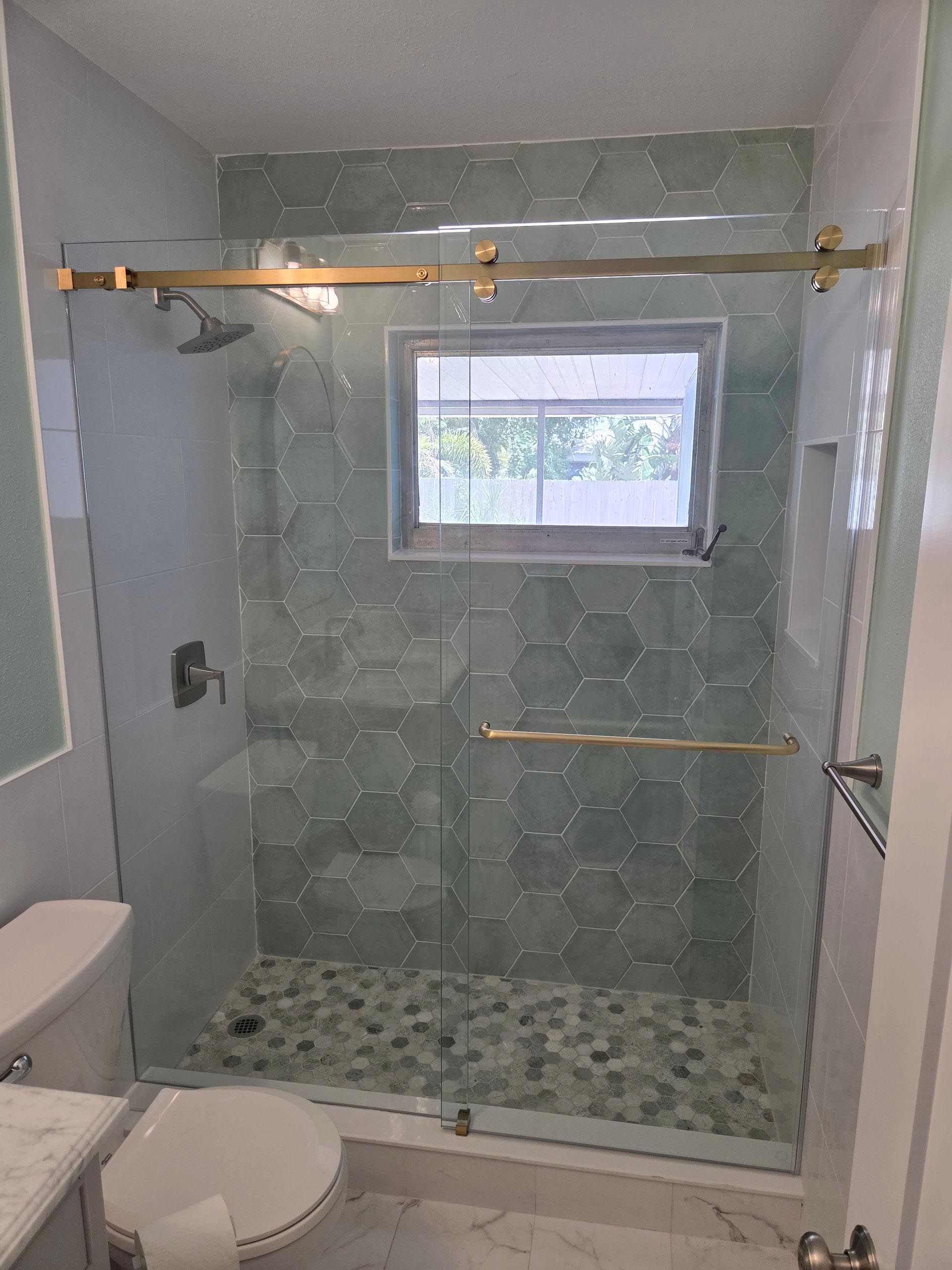 Bathroom with glass shower enclosure, green tile walls, and a small window above the shower