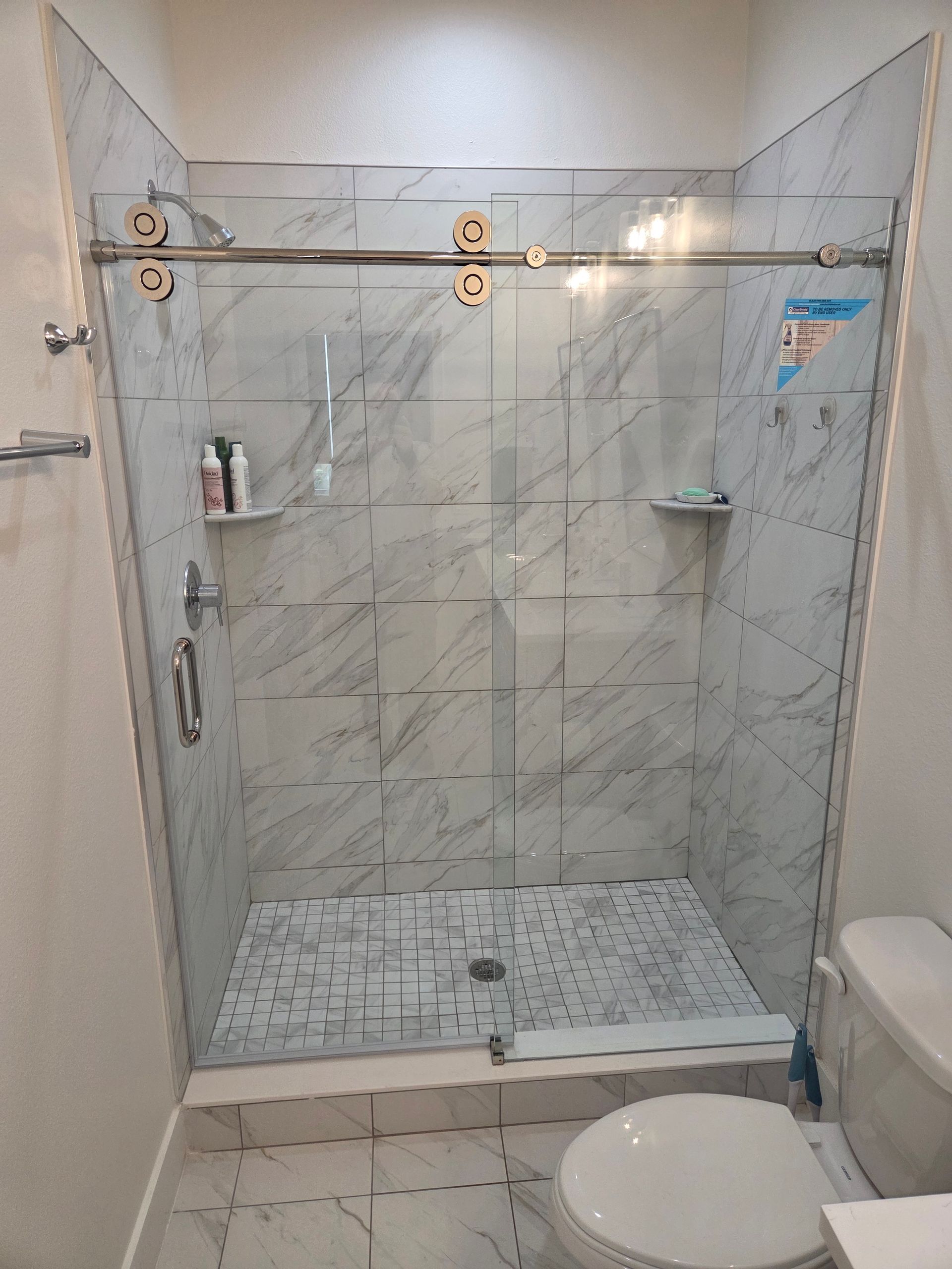 Glass-enclosed tiled shower with double doors, mosaic floor, and bathroom toilet visible on the right