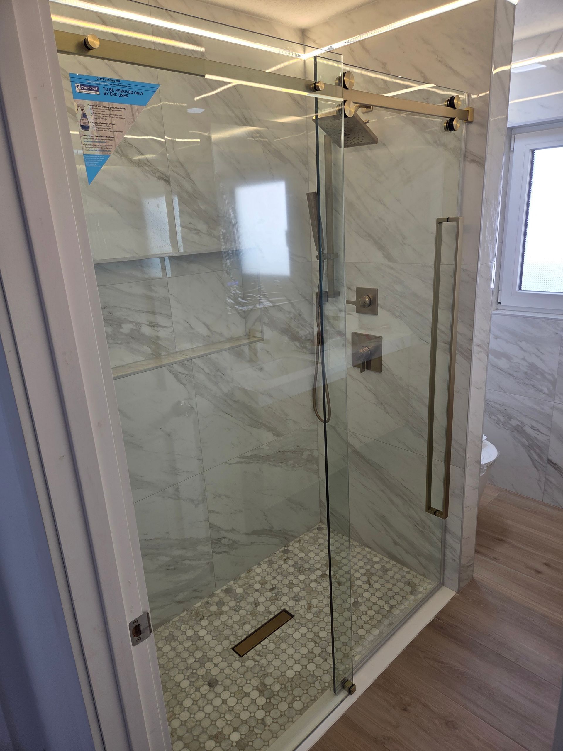 A modern shower with sliding glass doors, marble tile walls, and a pebble tile floor.