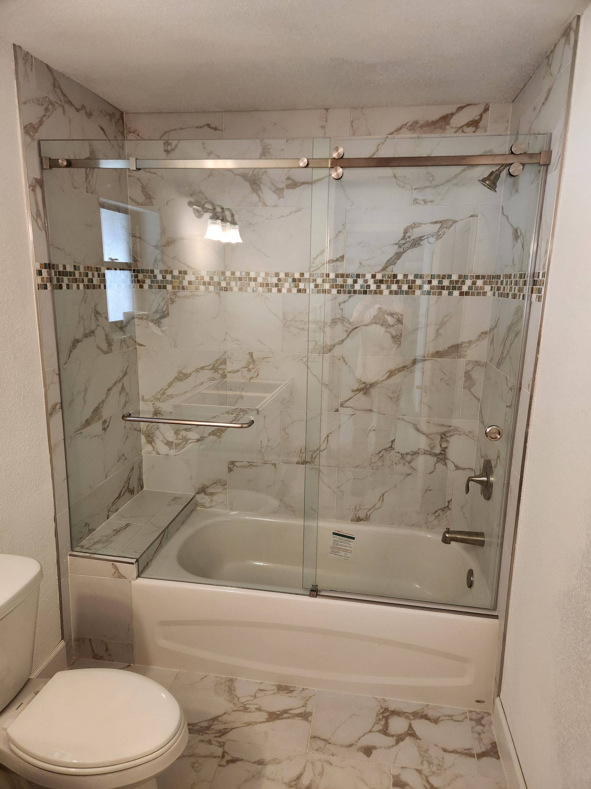 a bathroom with a bathtub, toilet, and sliding glass shower door