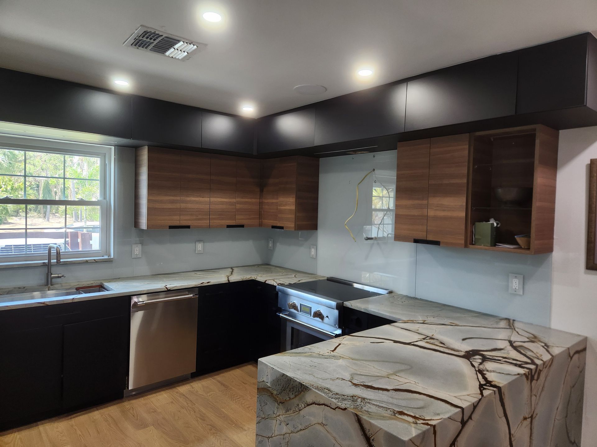 A kitchen with black cabinets , granite counter tops , stainless steel appliances and a large window.