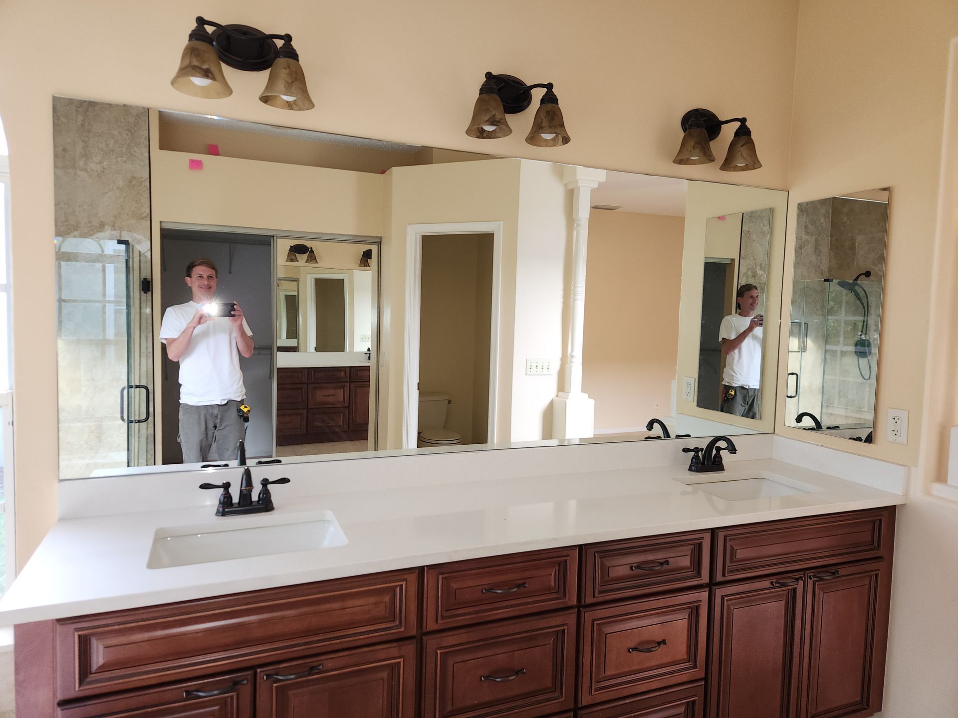 A bathroom with three mirrors above a double vanity, reflecting a person taking a photo.