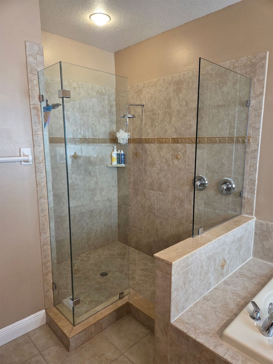 A corner shower with glass doors, tan tile, and chrome fixtures. A soap shelf holds toiletries.