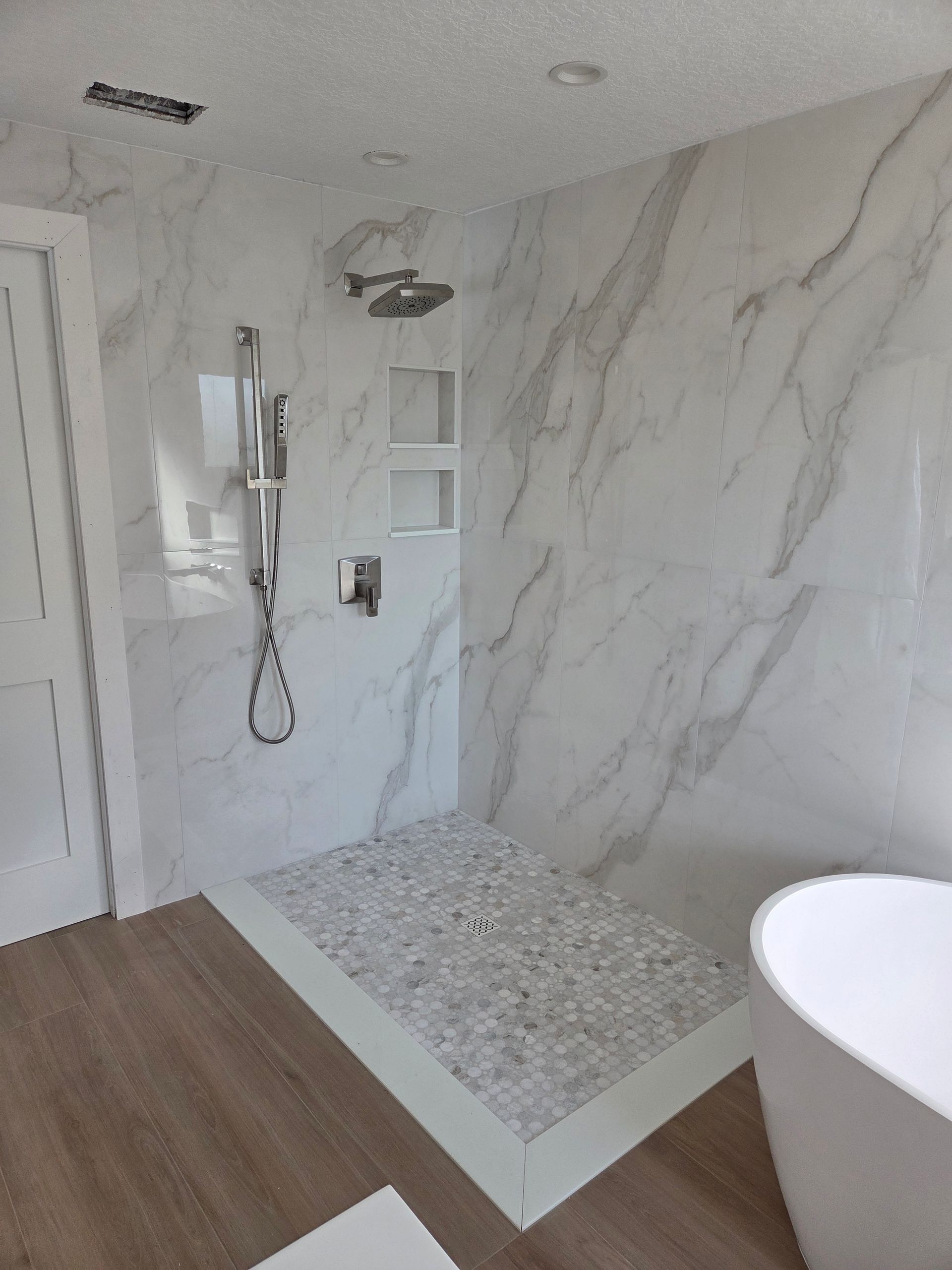 Modern shower with white marble-like tile walls, pebble floor, and rain shower head.