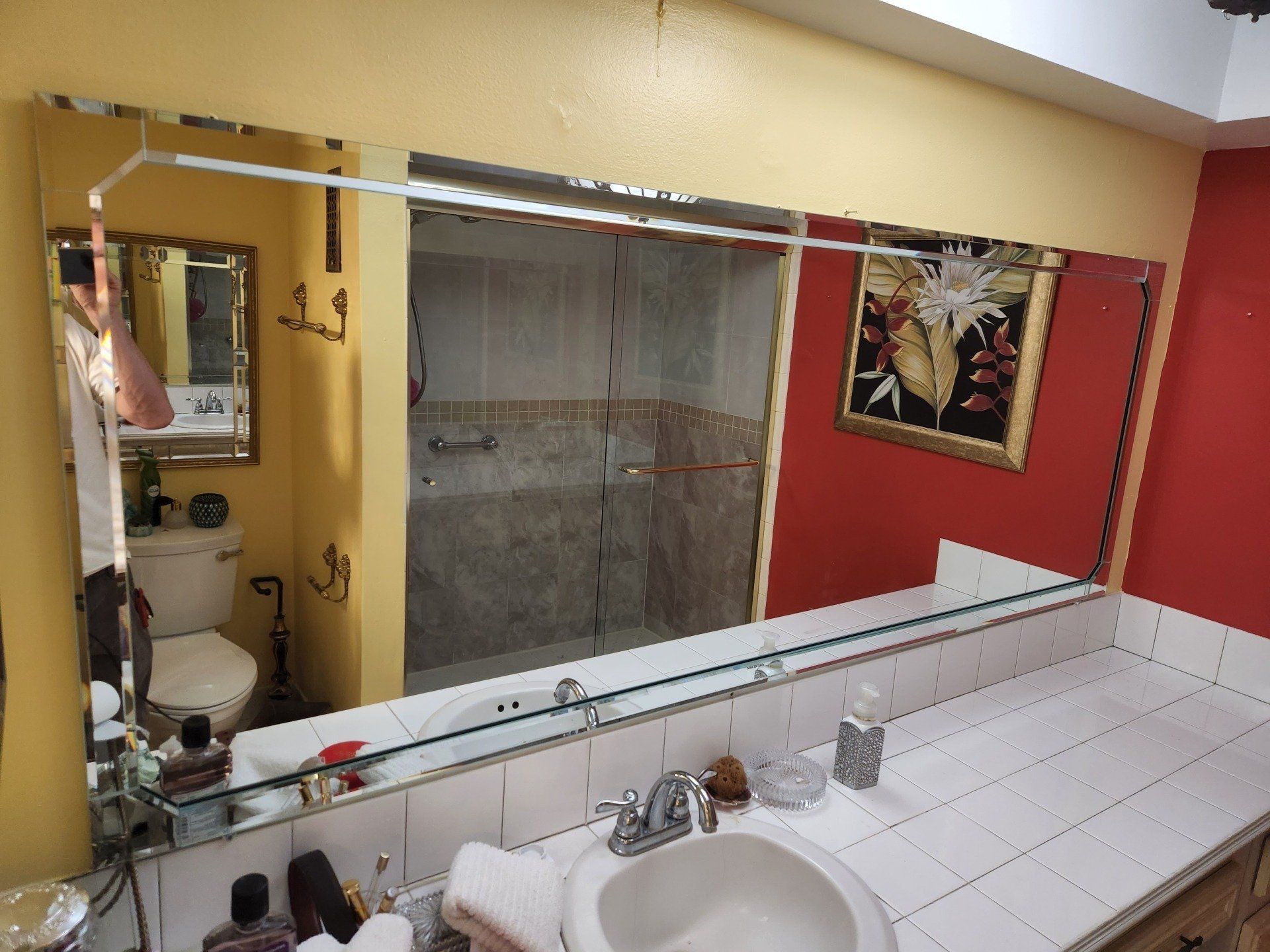 Bathroom with a large mirror reflecting sink, toilet, shower, and red and yellow walls.