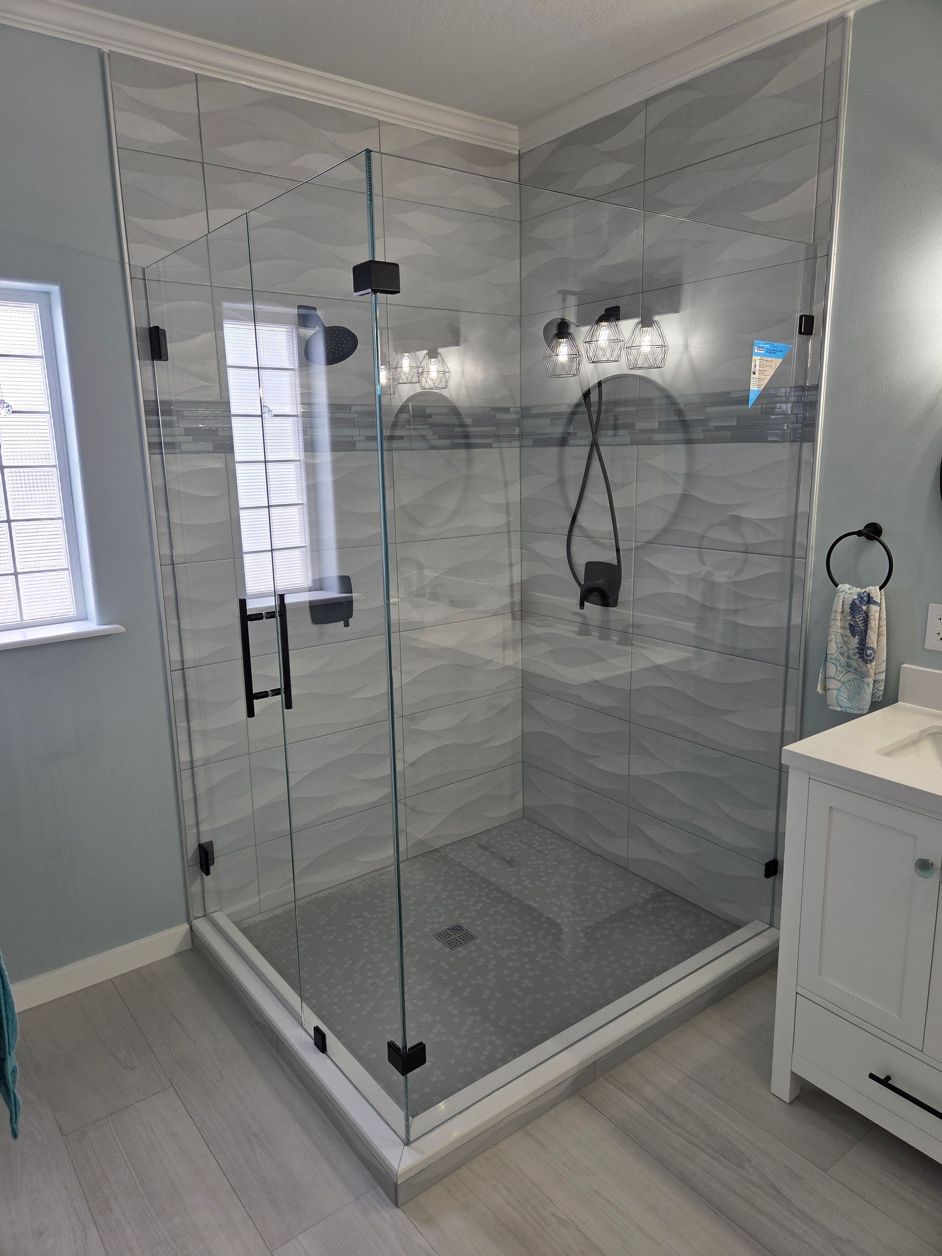 Glass-walled shower enclosure with light gray tile, black hardware, and a white cabinet.