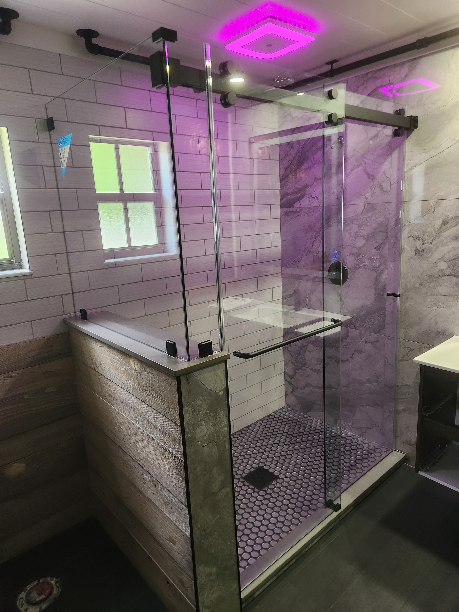 Modern shower with glass doors, black hardware, tile walls, and purple lighting.