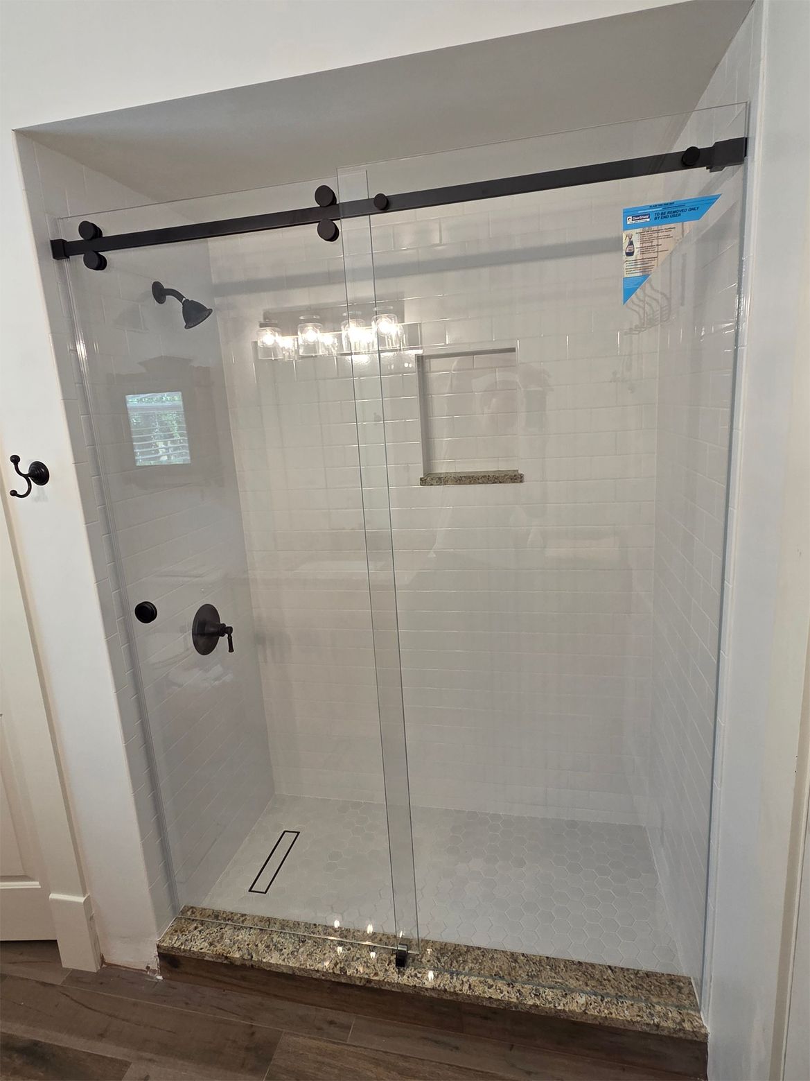 Glass shower with black sliding door hardware, white subway tile, and pebble flooring.