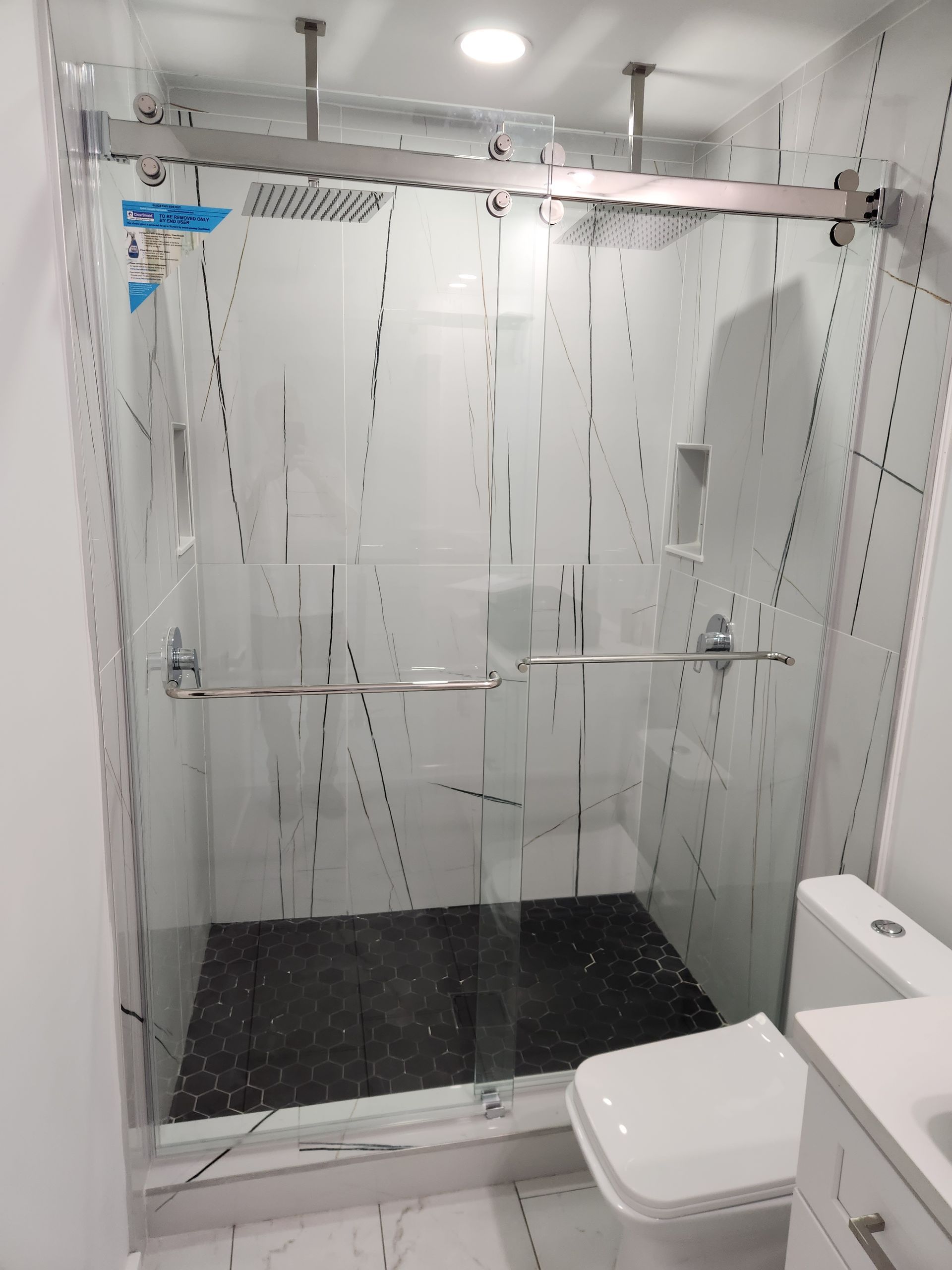 Shower with frosted glass doors and black tiled floor. Includes a toilet and marble-patterned walls.