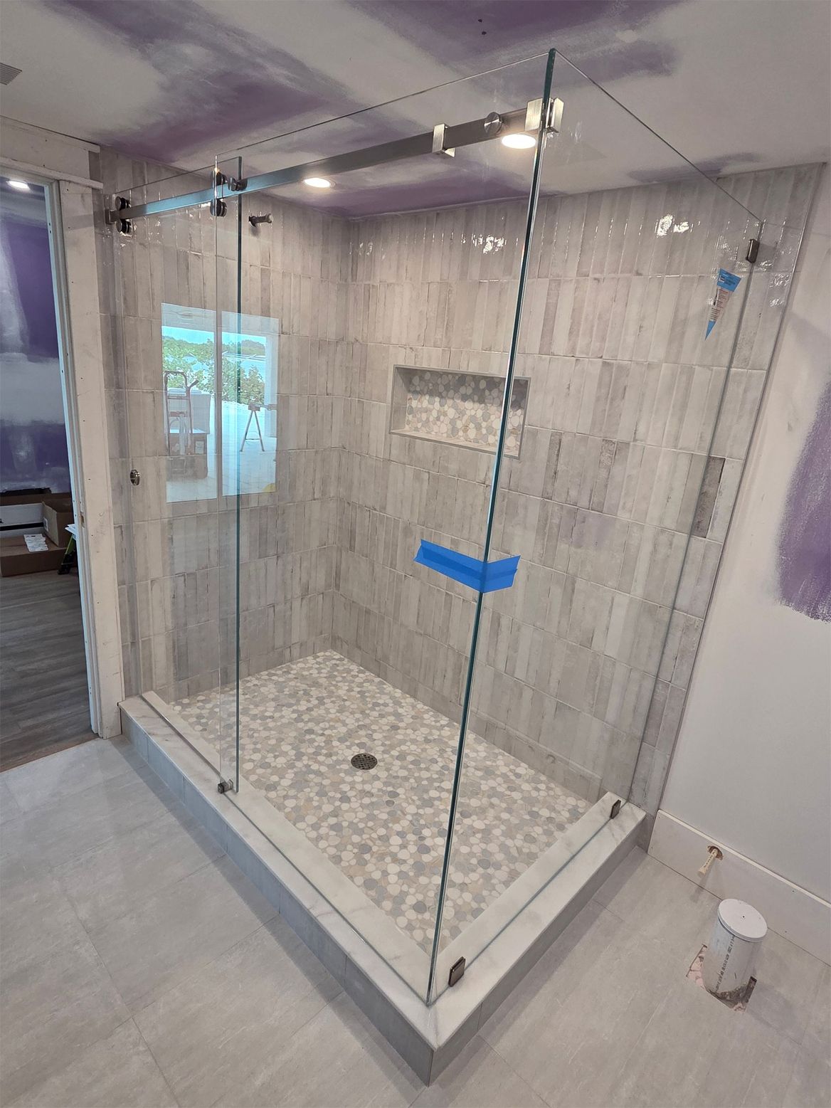 Glass shower enclosure with gray tiled walls and pebble floor.