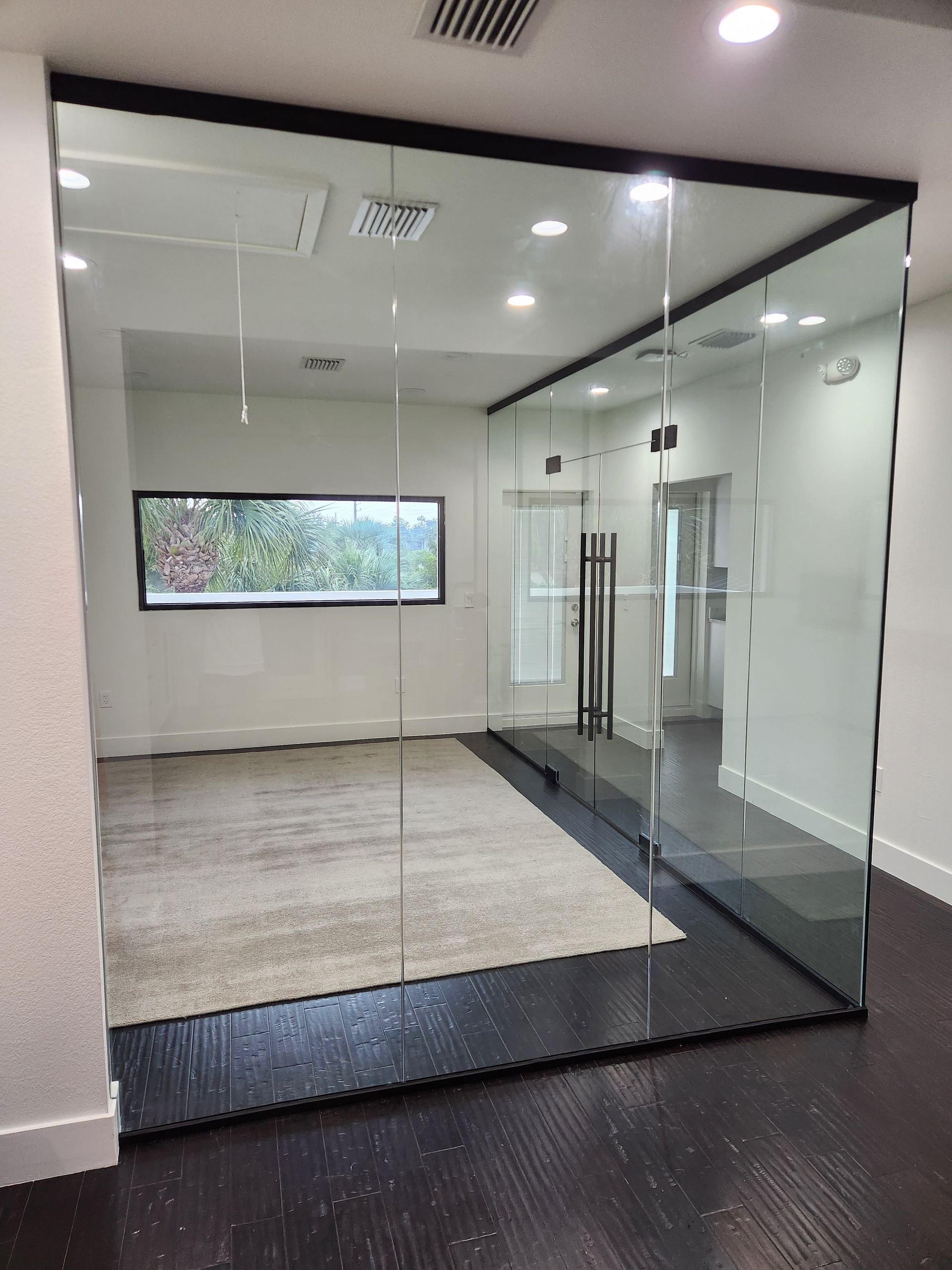 Glass-walled office with dark trim, dark wood floor, and a light-colored rug inside.