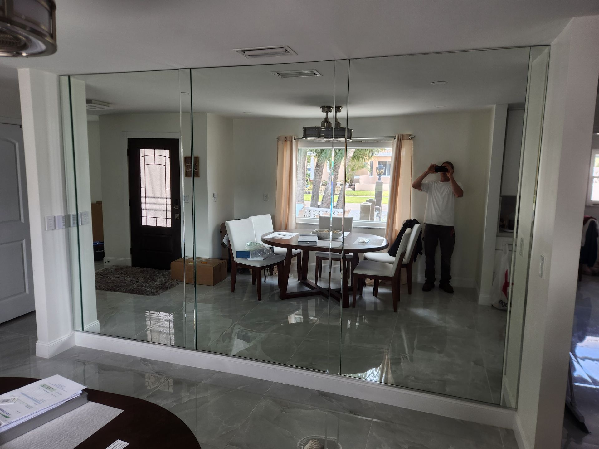 A man is standing in front of a large mirror in a dining room.