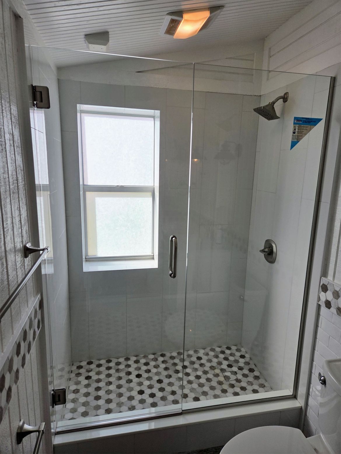 Bathroom with glass shower enclosure, white tile, and black and white floor tile.
