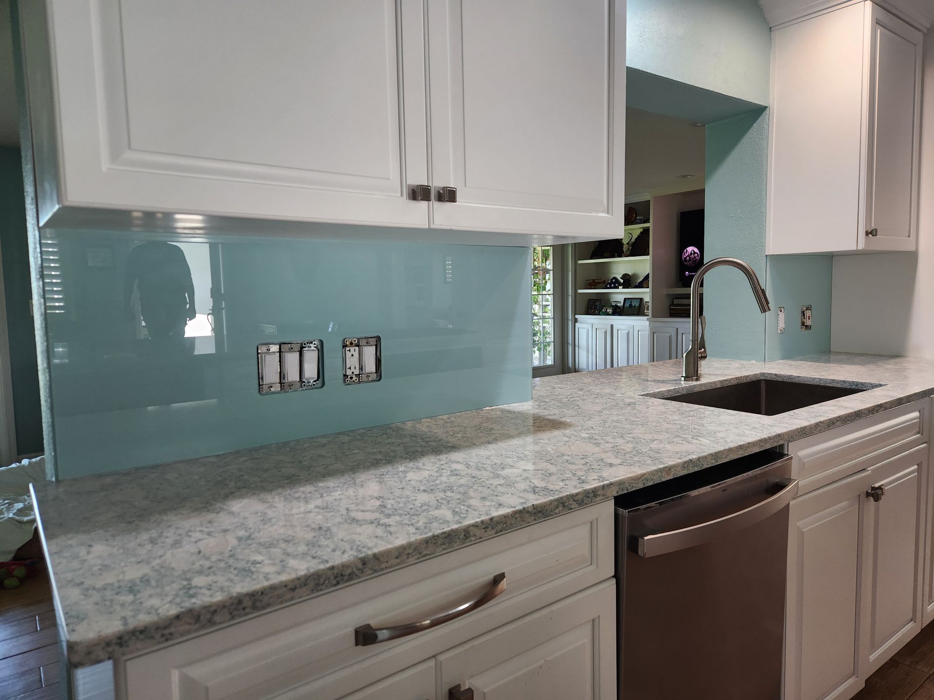 A kitchen with white cabinets, granite countertops, a sink, and a stainless steel dishwasher.