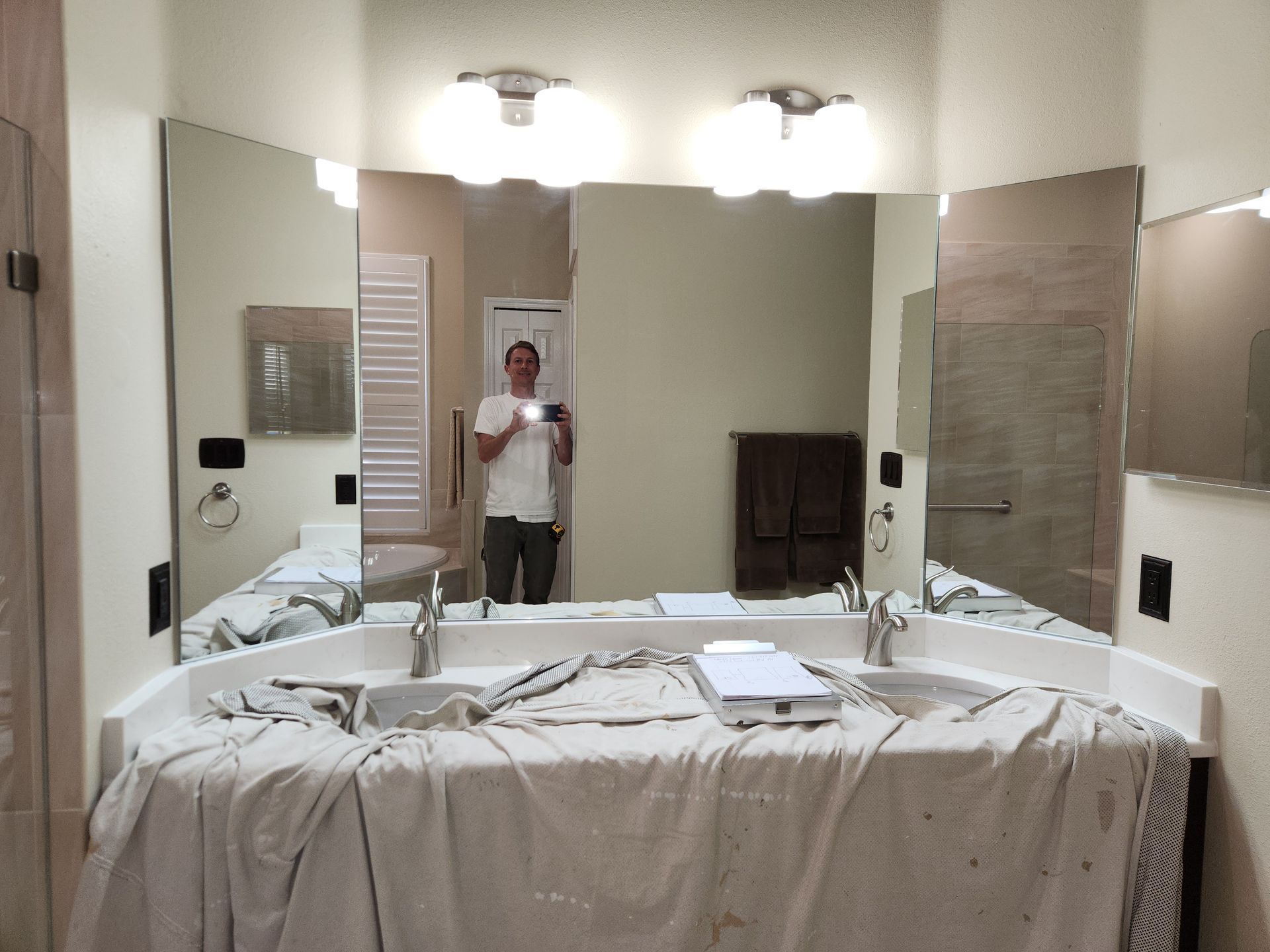 Person taking a photo in a bathroom mirror with a covered counter, two sinks, and overhead lights.