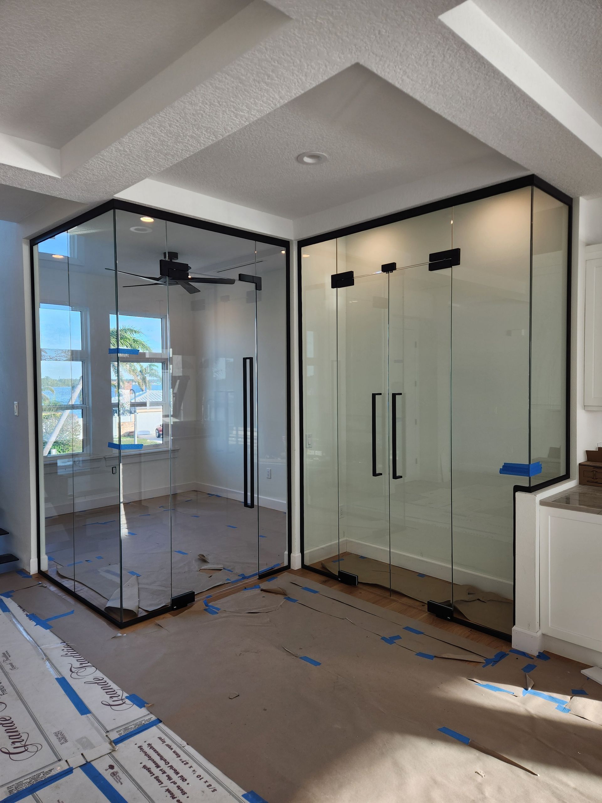 Two glass enclosed spaces with black frames, likely offices or showers, in a modern interior setting.