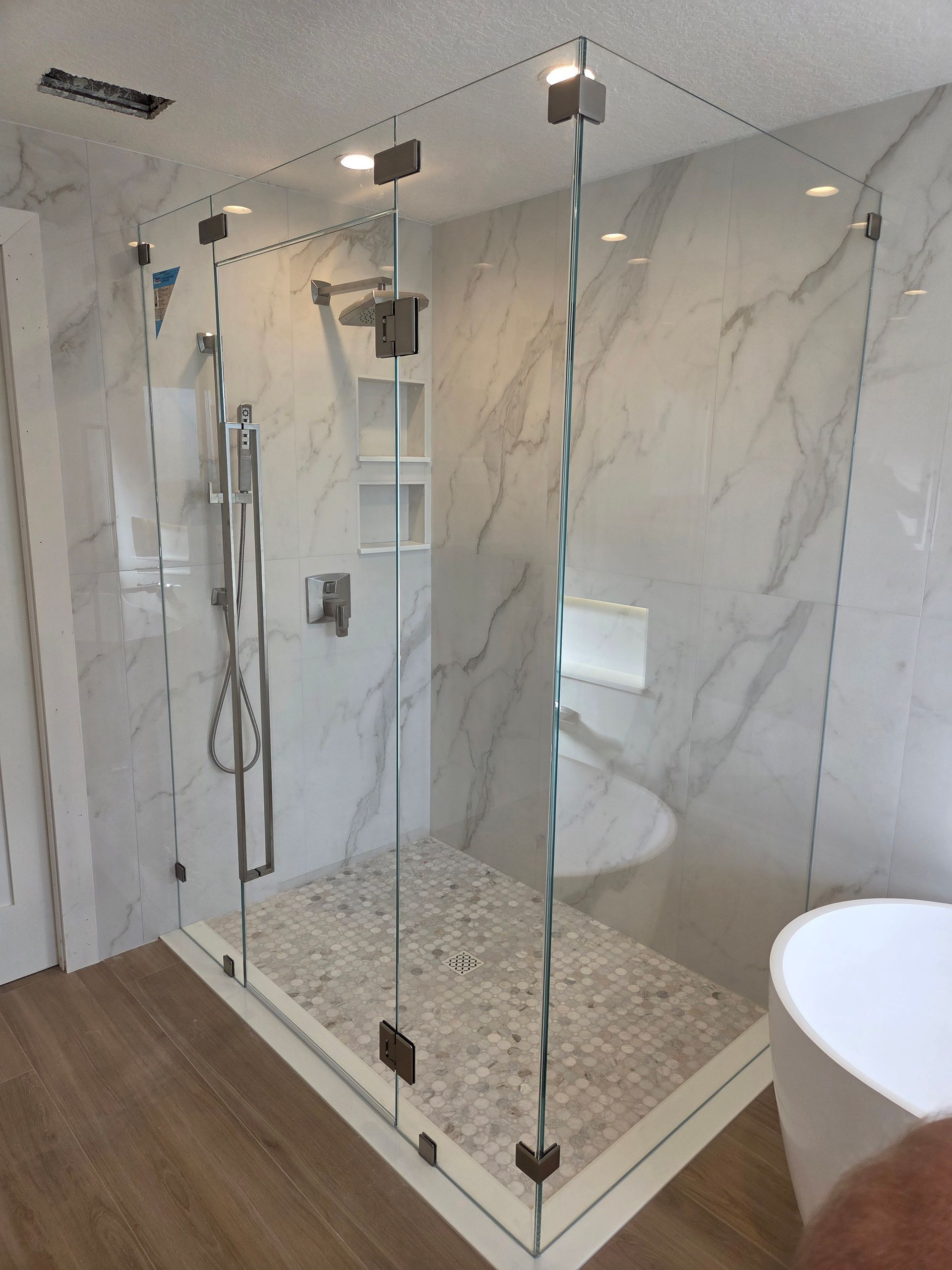 Glass shower enclosure with gray marble tile walls, pebble floor, and chrome fixtures.