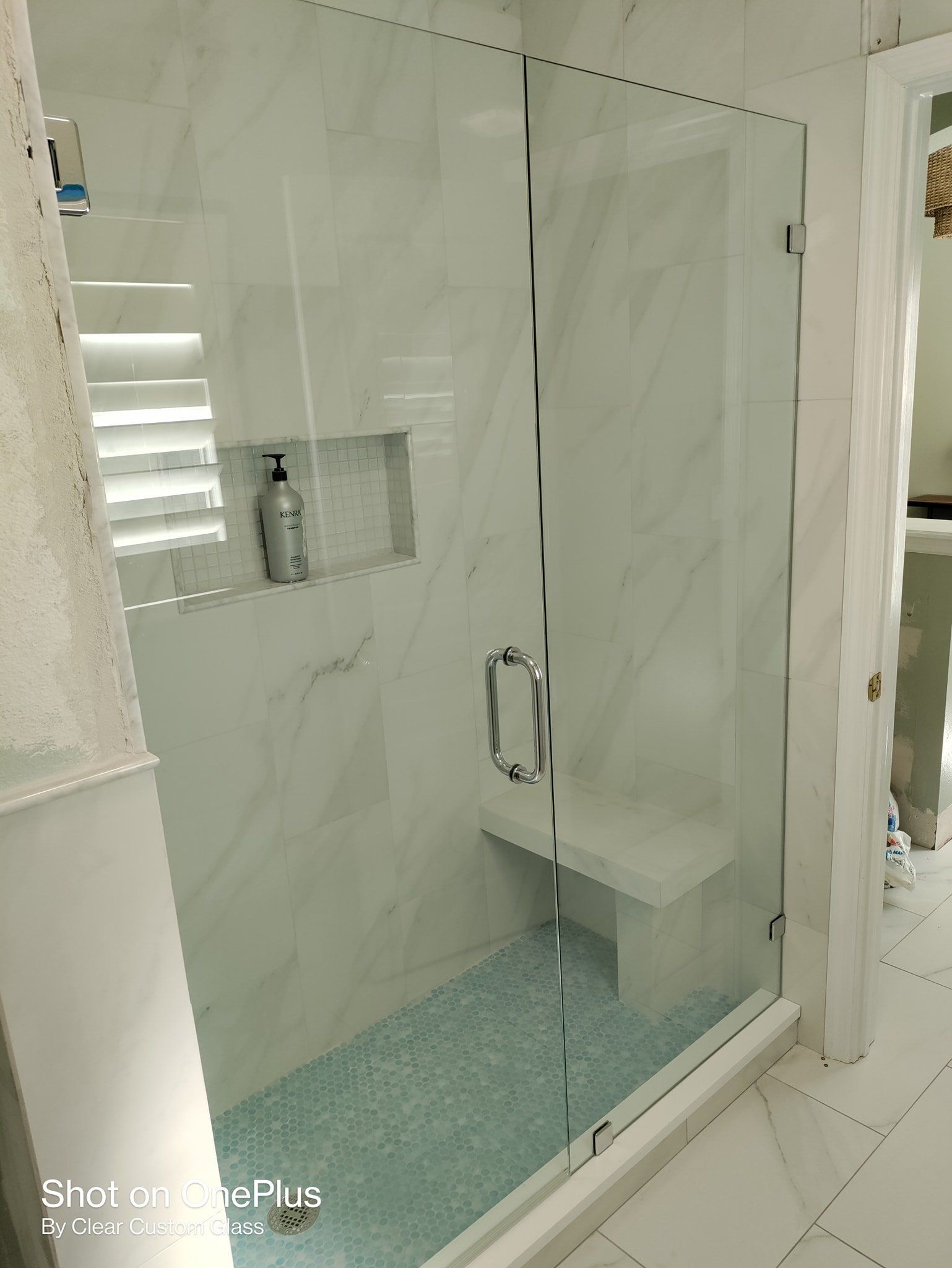 A modern bathroom shower with marble tile, a glass door, and a built-in bench seat.