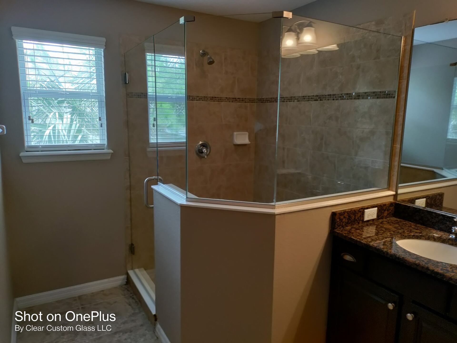 Modern bathroom with glass shower, tan tile, and granite countertop, with windows and a sink.