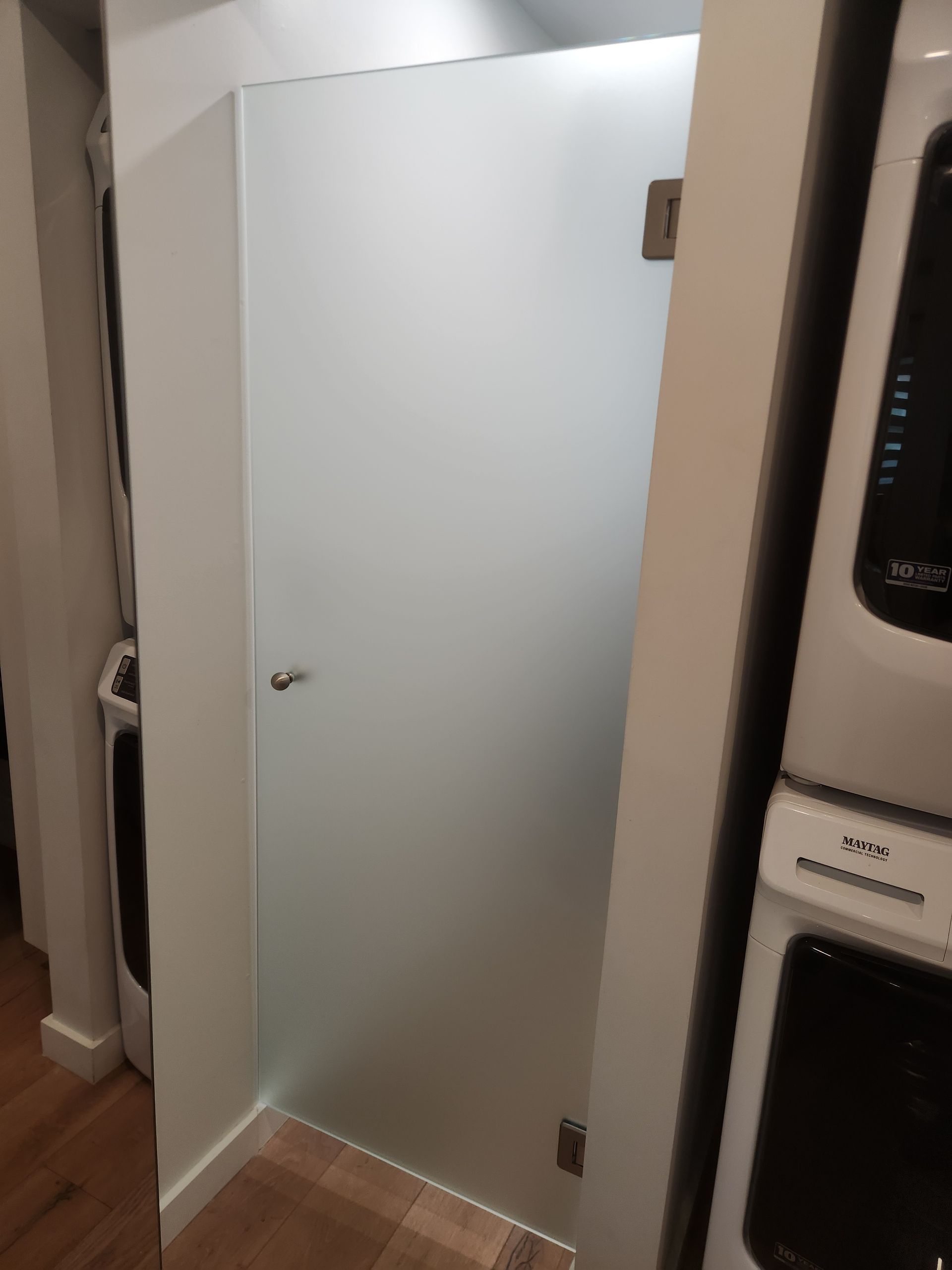 A bathroom with a glass shower door and a stack of washers and dryers.