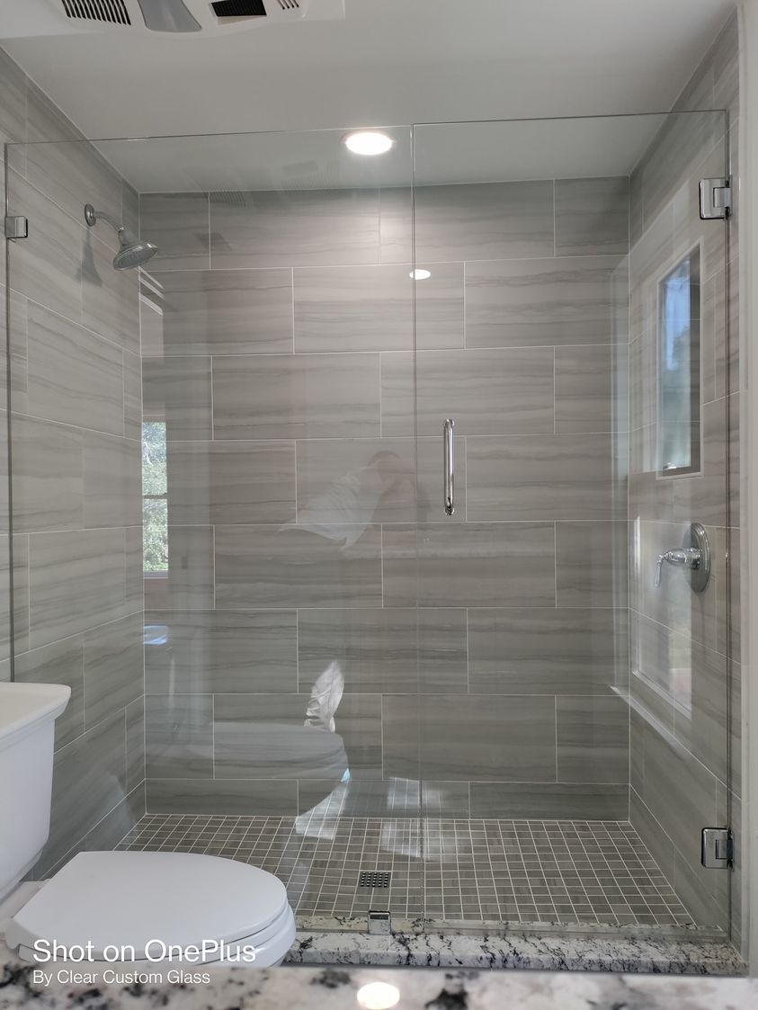 Modern bathroom with gray tiled shower, glass doors, and toilet.