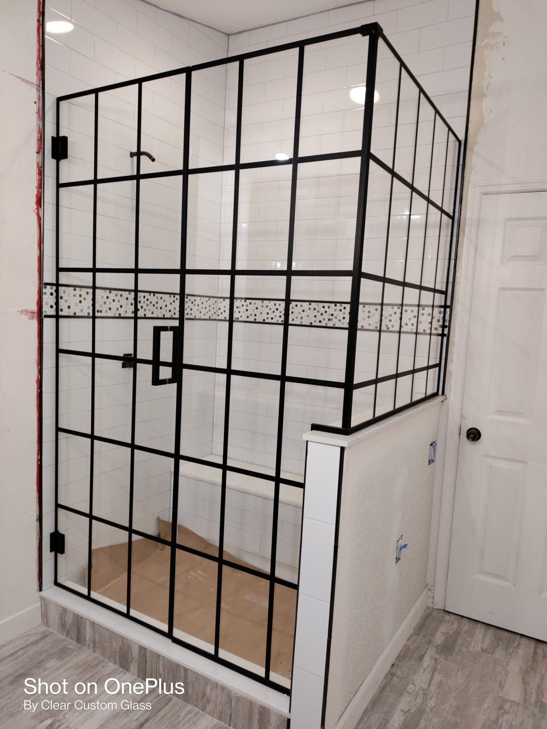 Black-framed glass shower enclosure with grid design. White walls, door, and light-colored tiled floor.