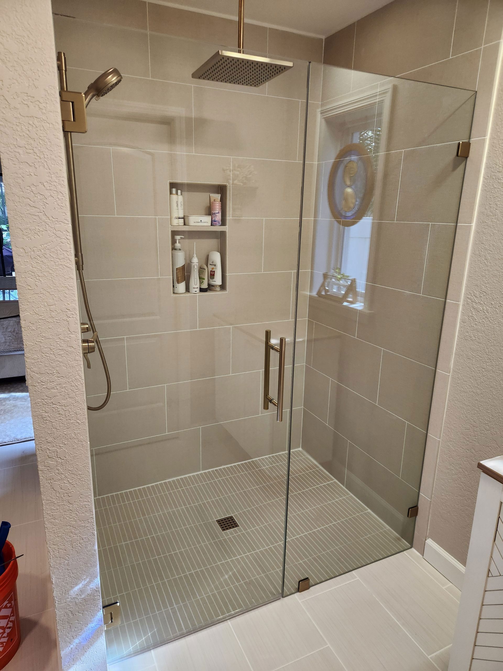 Modern shower with glass enclosure, gray tile, gold fixtures, and built-in shelving.