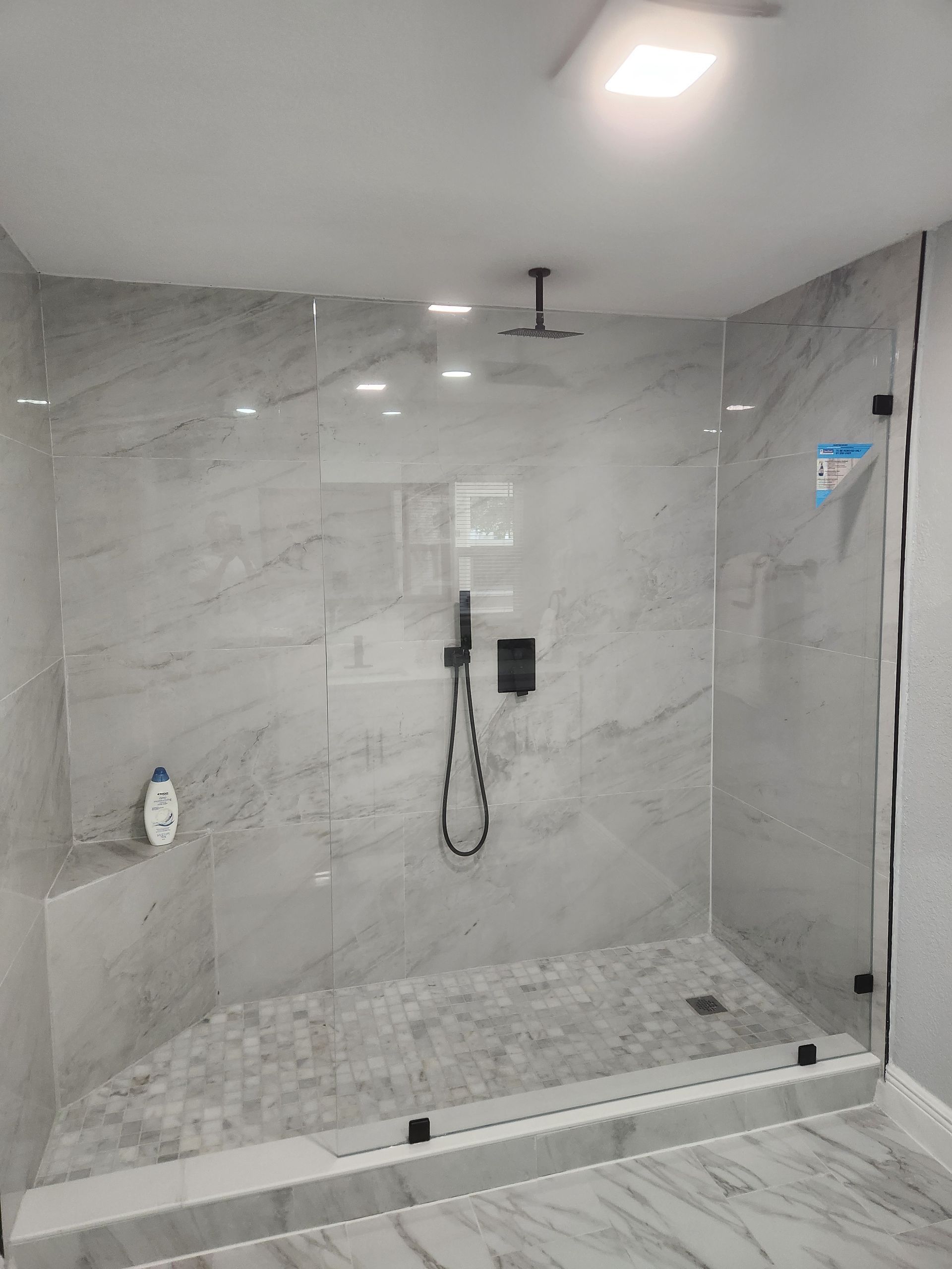 Modern shower with marble tiles, glass doors, and black fixtures.