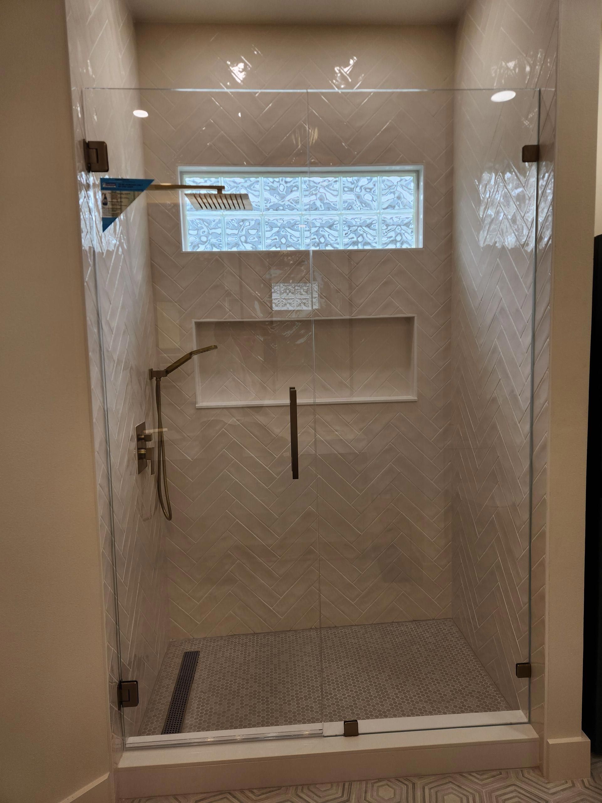 Glass shower with bronze hardware, pebble floor, white tile, and rectangular window.