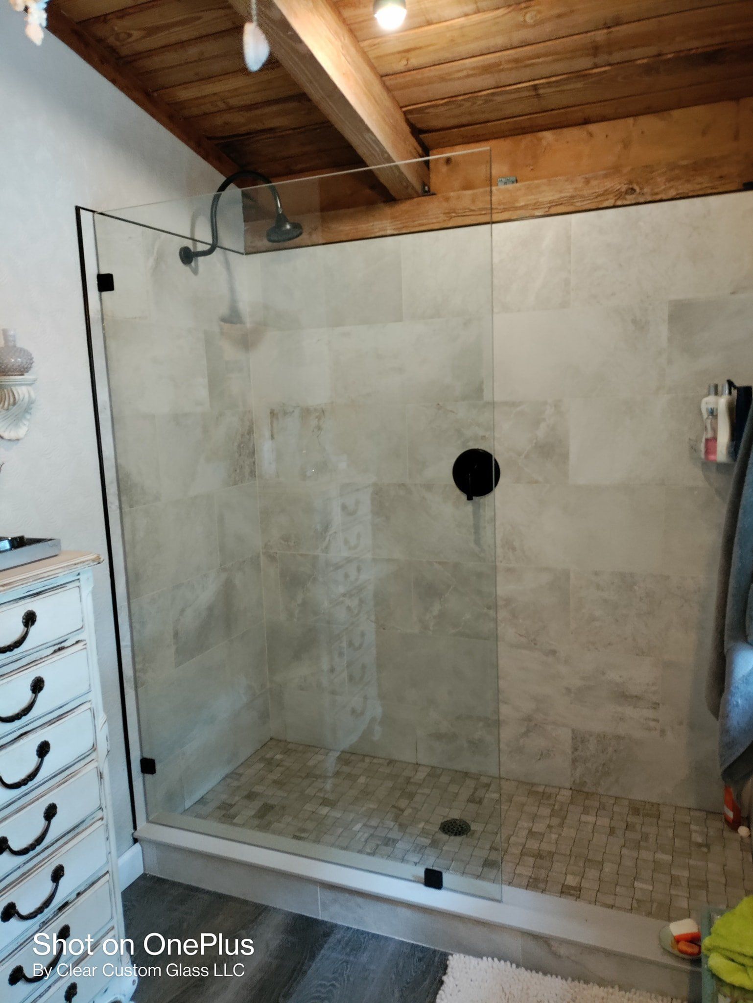 Shower with stone tile walls, glass door, dark fixtures, and wooden ceiling.